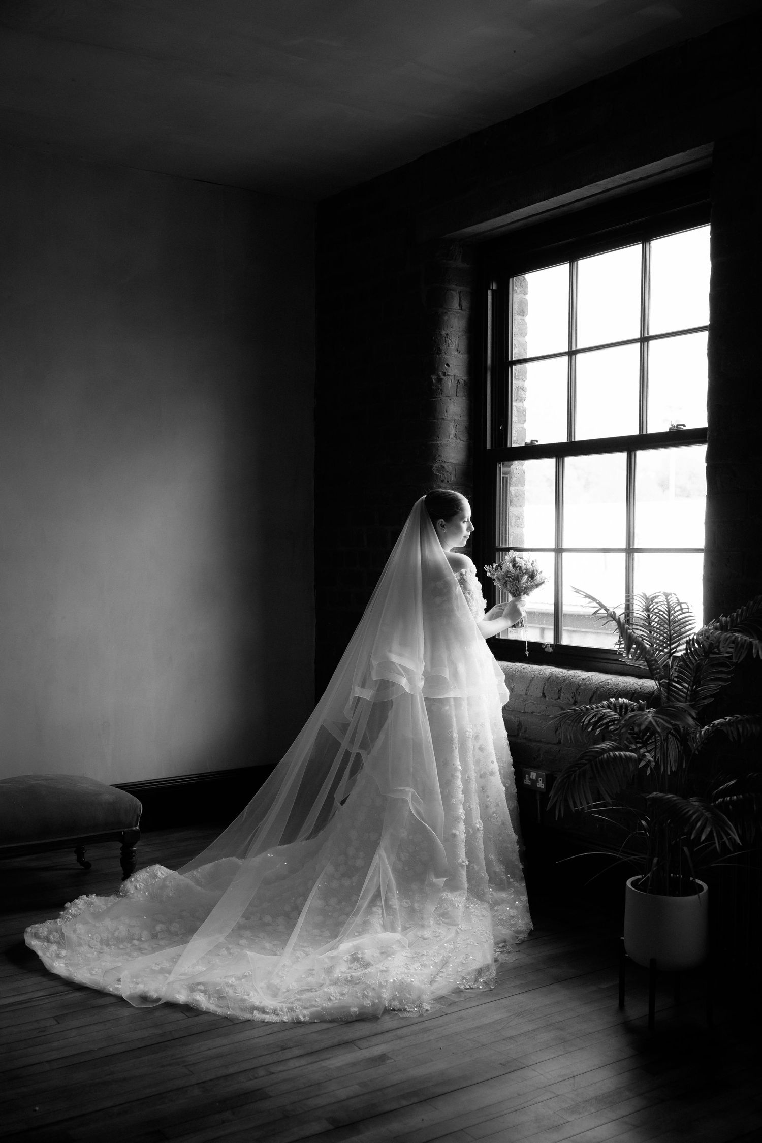 A dramatic black and white photo series shows a bride in a flowing veil and gown standing by a window in an empty room.