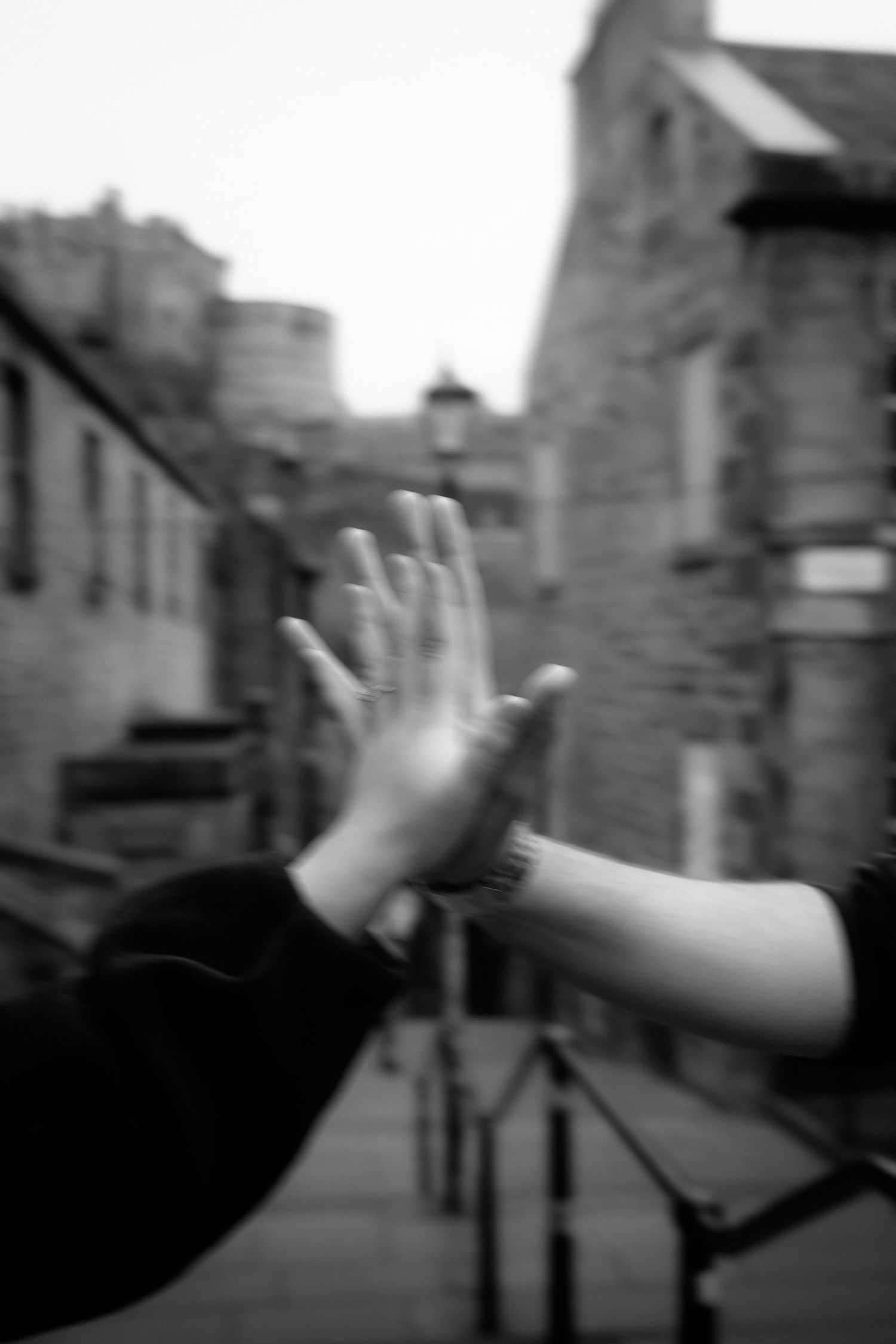 Two hands pressing together in a high-five gesture on a blurred black and white urban street background.