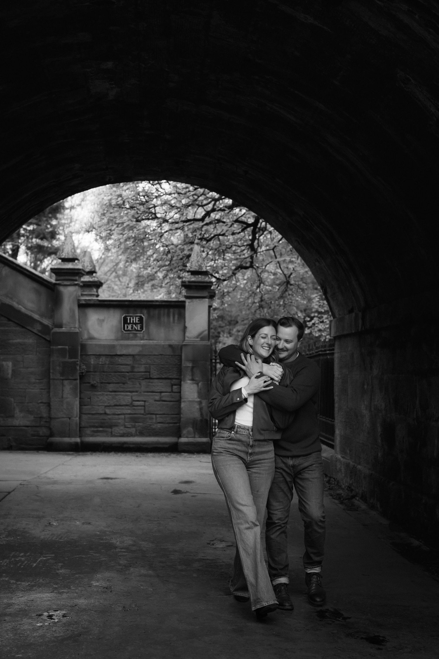 Black and white photo of a couple embracing under a stone arch tunnel in Central Park, New York.