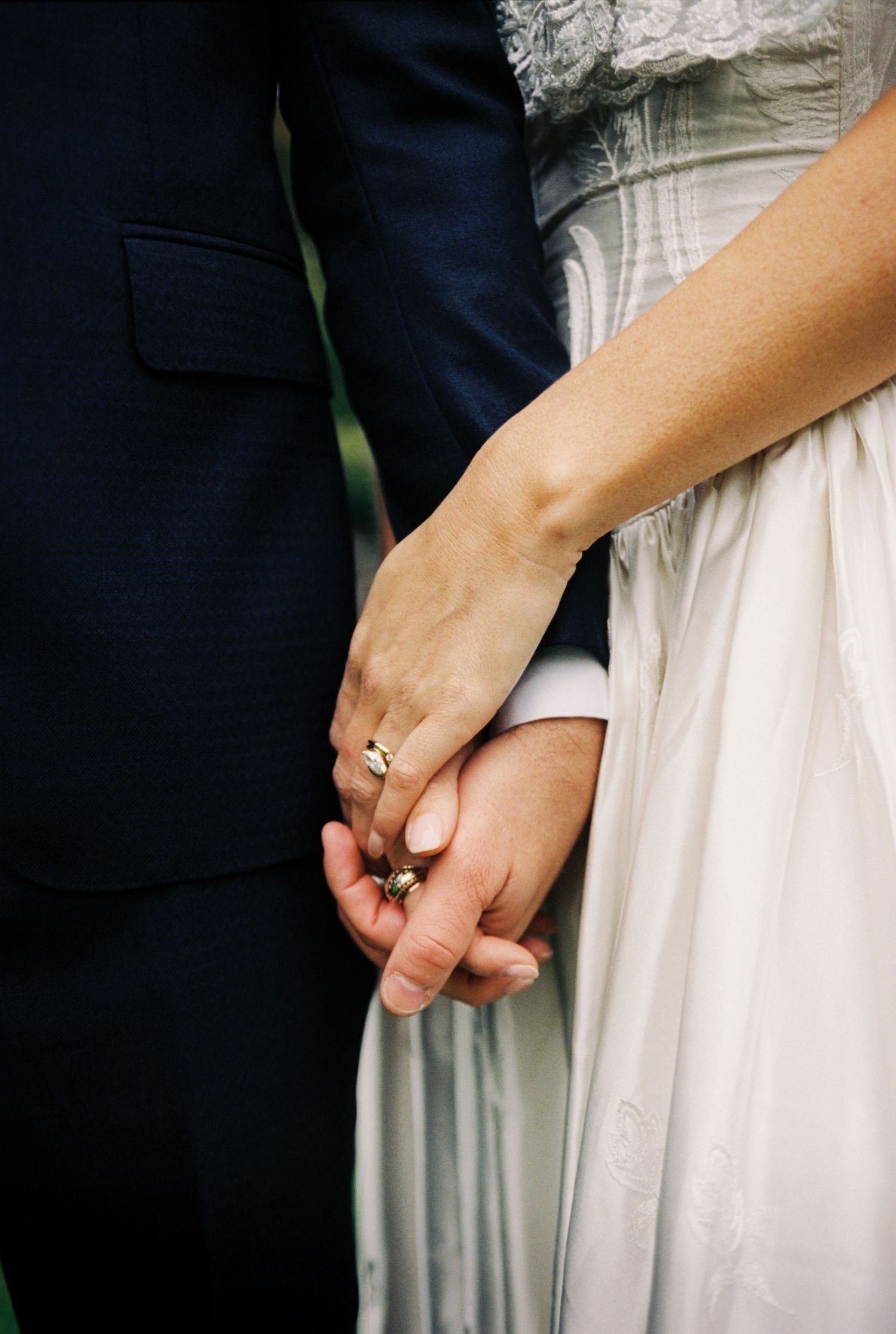 A close-up series of hands holding each other tenderly in wedding attire with white dress and dark suit details.