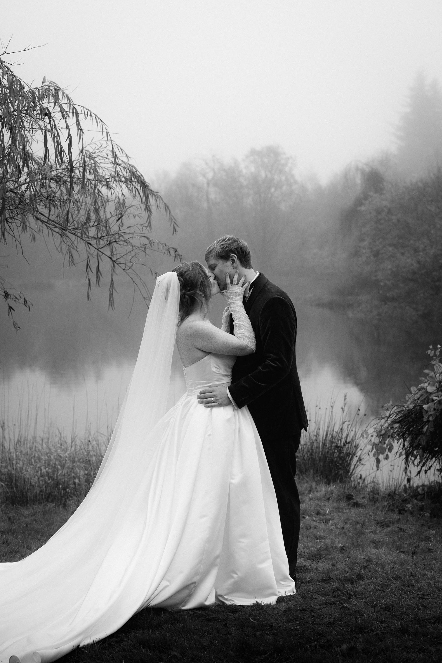 Romantic black and white wedding portraits by a misty lake with flowing white dress and veil.