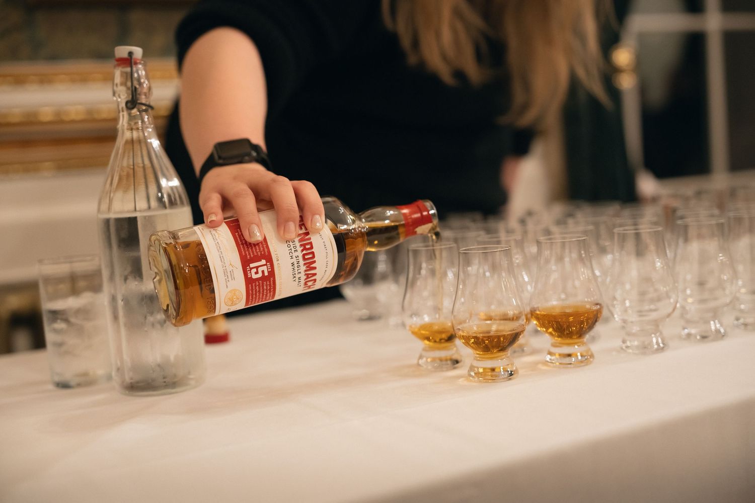 Bartender pouring amber colored liquor into a glass at an elegant bar counter with crystal glassware.