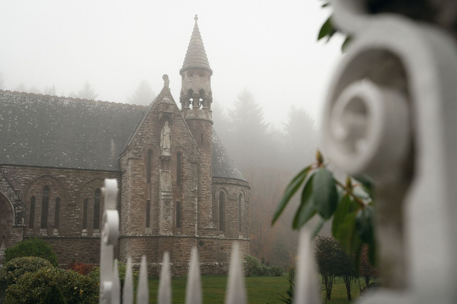A historic stone church with a tall spire stands in a misty landscape with gothic architectural details.