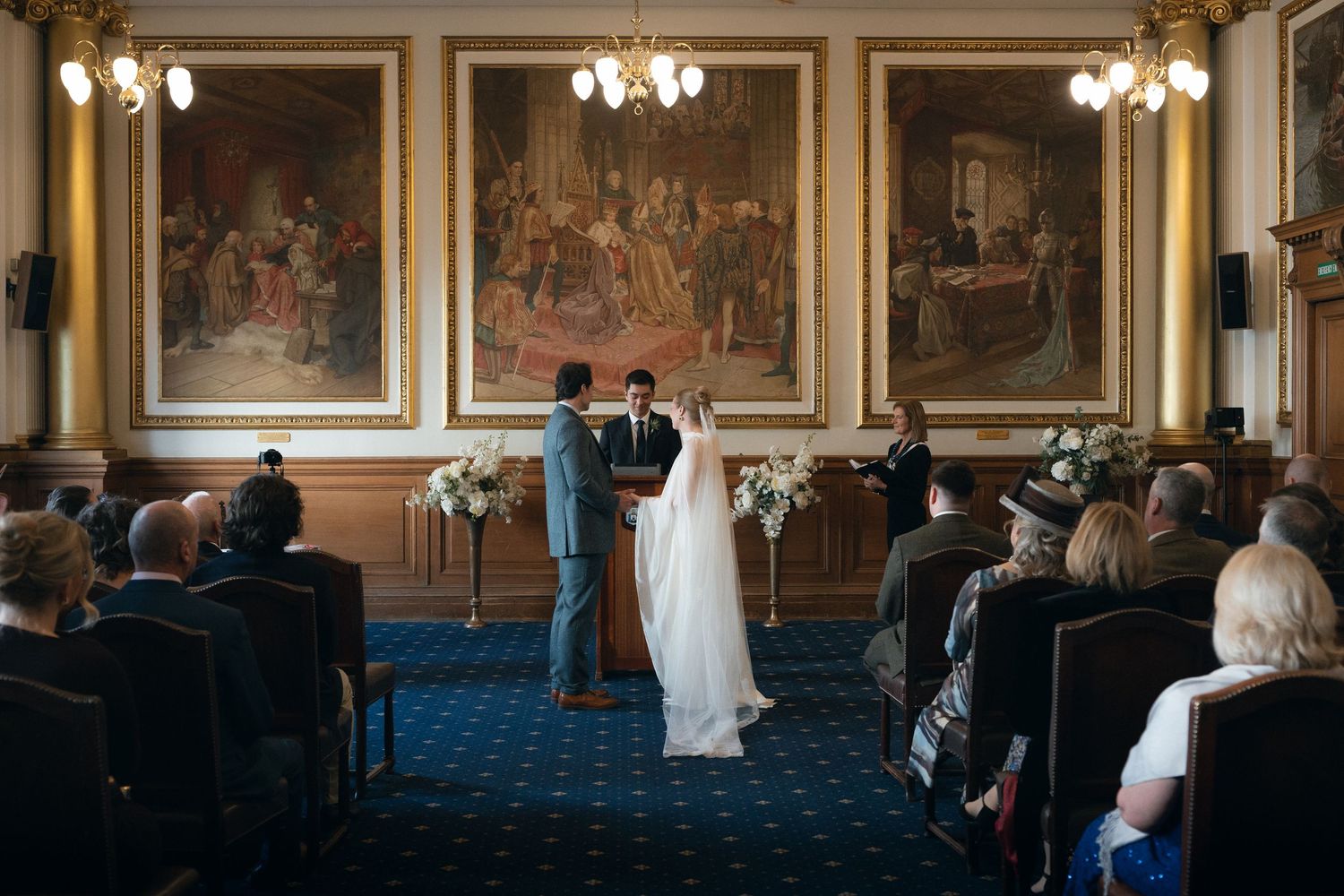 Elegant chandelier-lit ballroom with ornate gold frames and blue carpet during an indoor event.