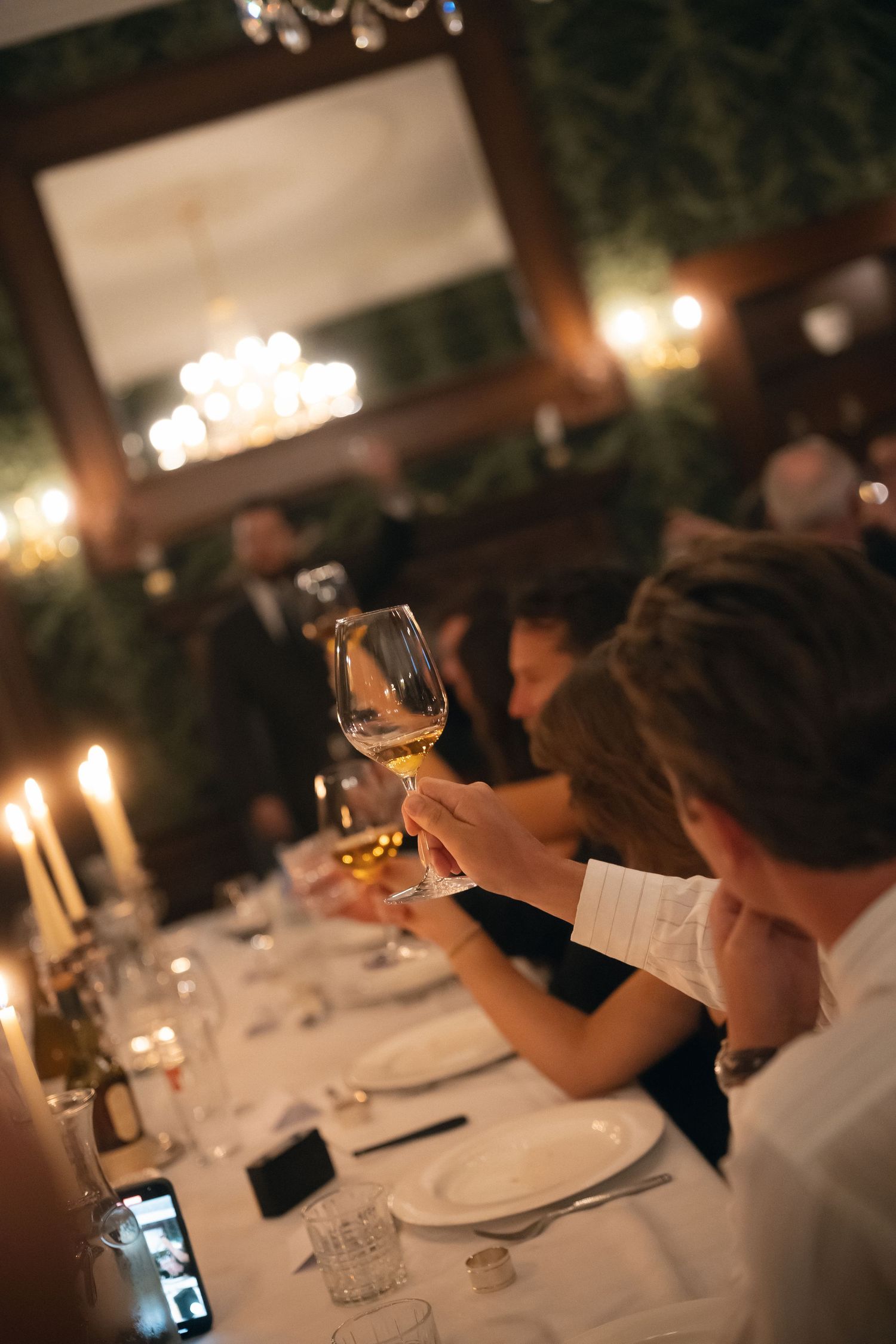 People raise wine glasses in a dimly lit restaurant during an elegant dinner service.