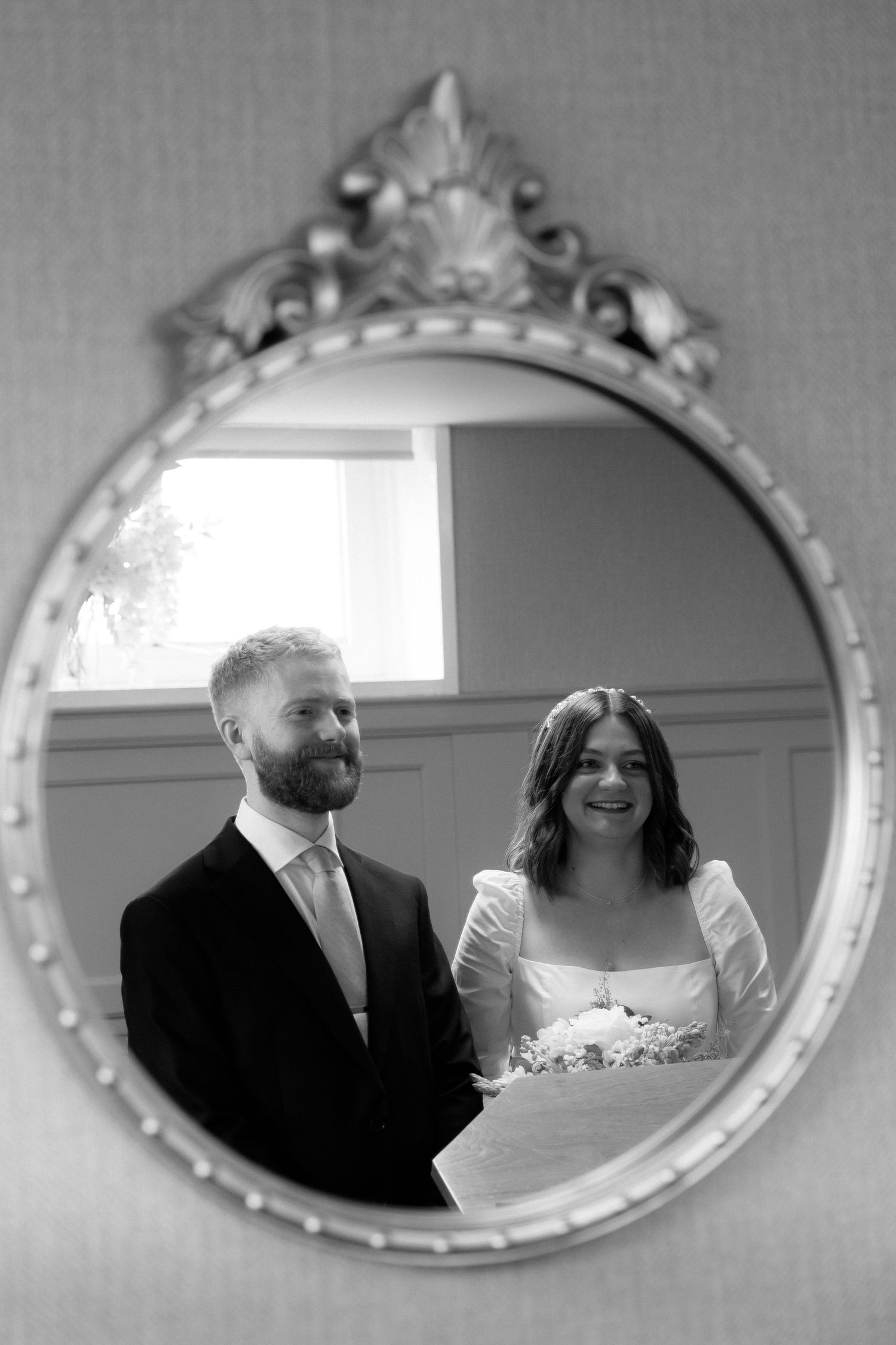 A series of five oval mirrors on a wall reflect moments from a wedding celebration in black and white.