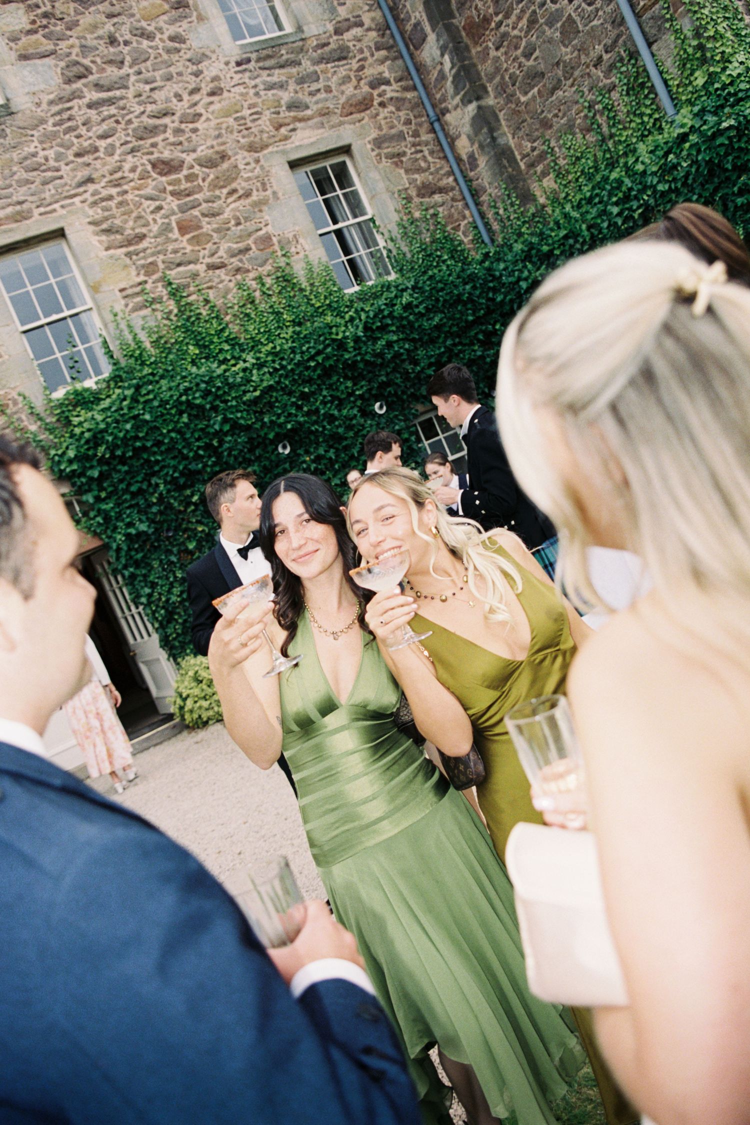 A sequence of candid wedding reception photos showing guests laughing and enjoying themselves against a stone building exterior.