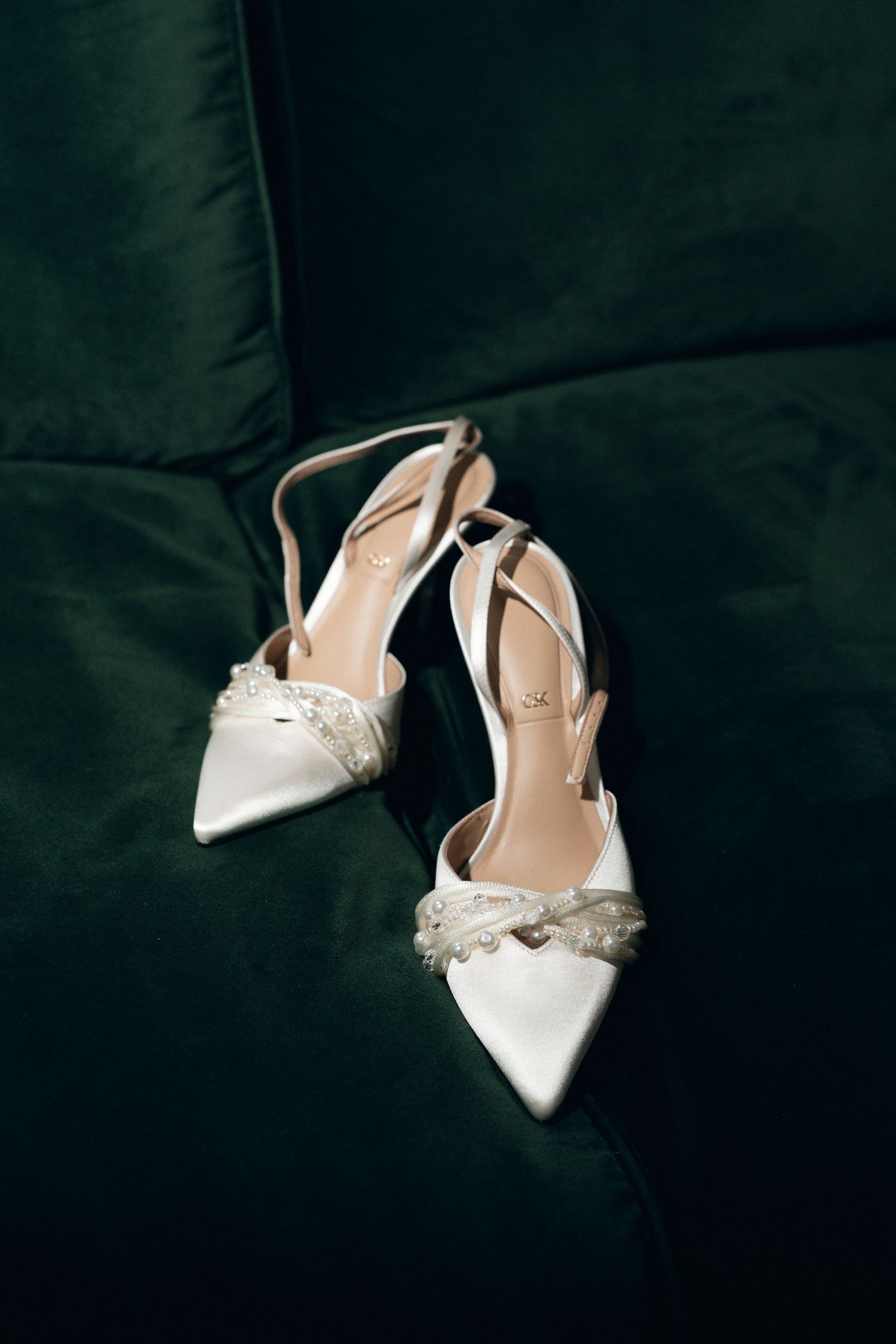 Elegant white satin bridal slingback heels with crystal embellishments photographed against a dark background.