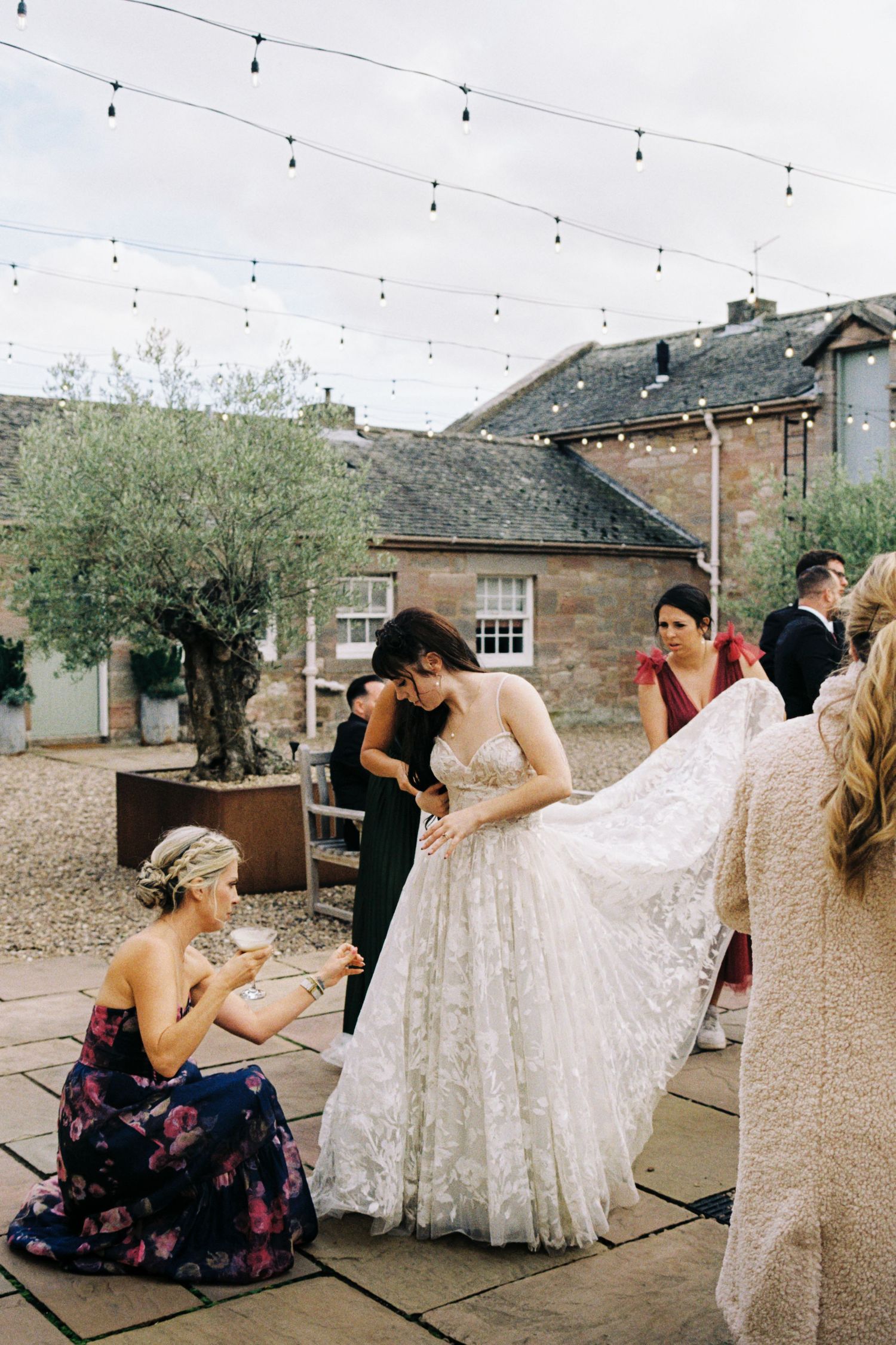 A series of wedding preparation photos showing attendants helping with a white wedding dress outdoors.