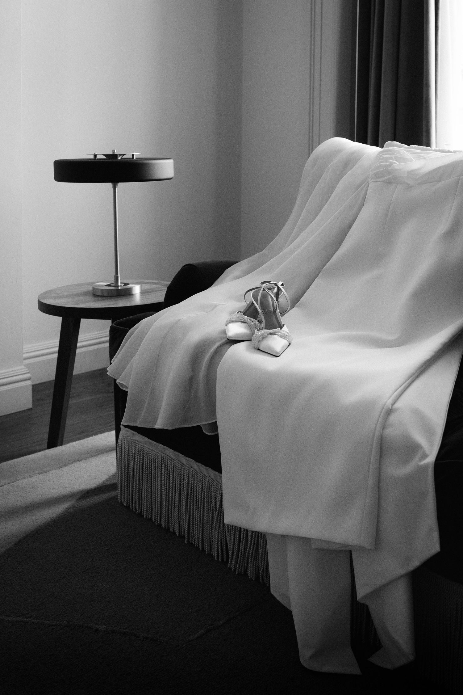 Black and white photo series of a white draped fabric on a chair next to a table lamp creating dramatic shadows.