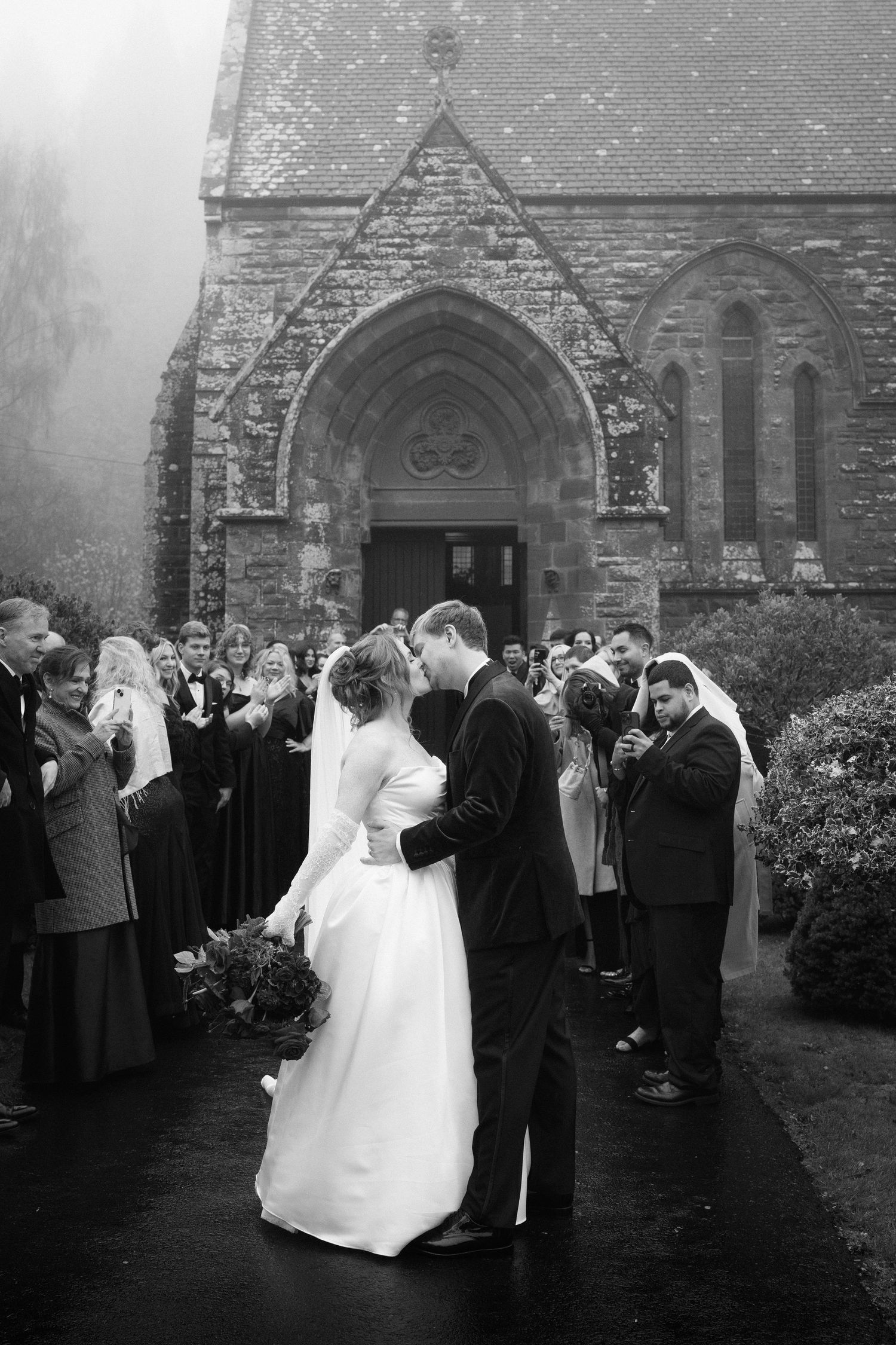 A wedding ceremony sequence showing a couple and guests outside a stone church building in black and white photography.