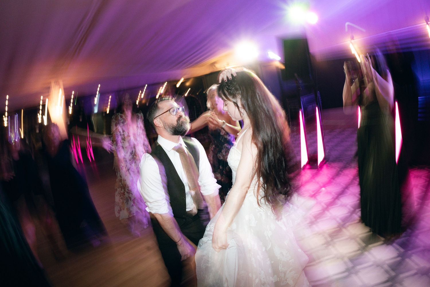 Motion-blurred dance floor scene at a wedding reception with purple lighting and spinning dancers.