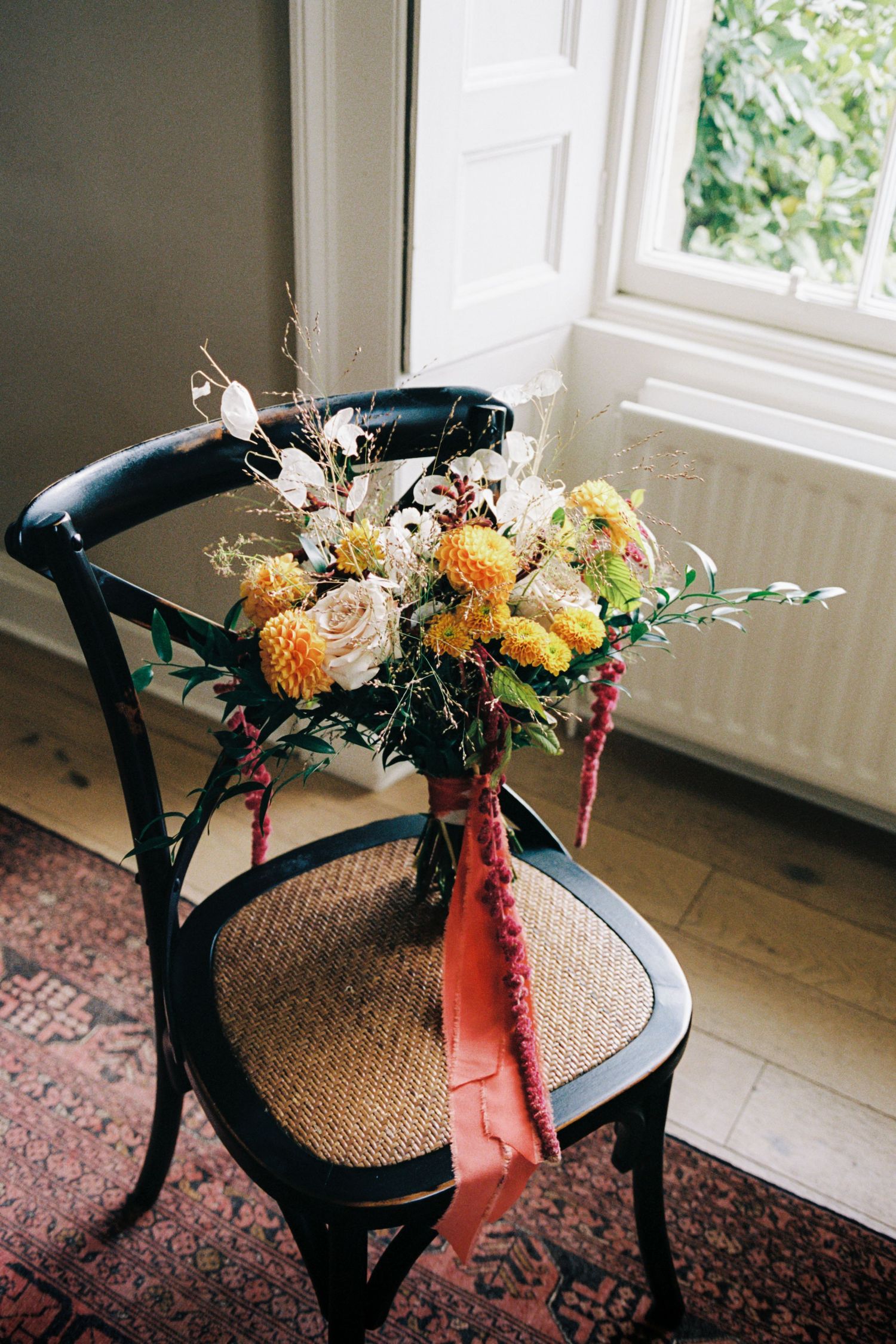 Vintage black chair with woven seat decorated with peach and orange floral arrangement by a window.
