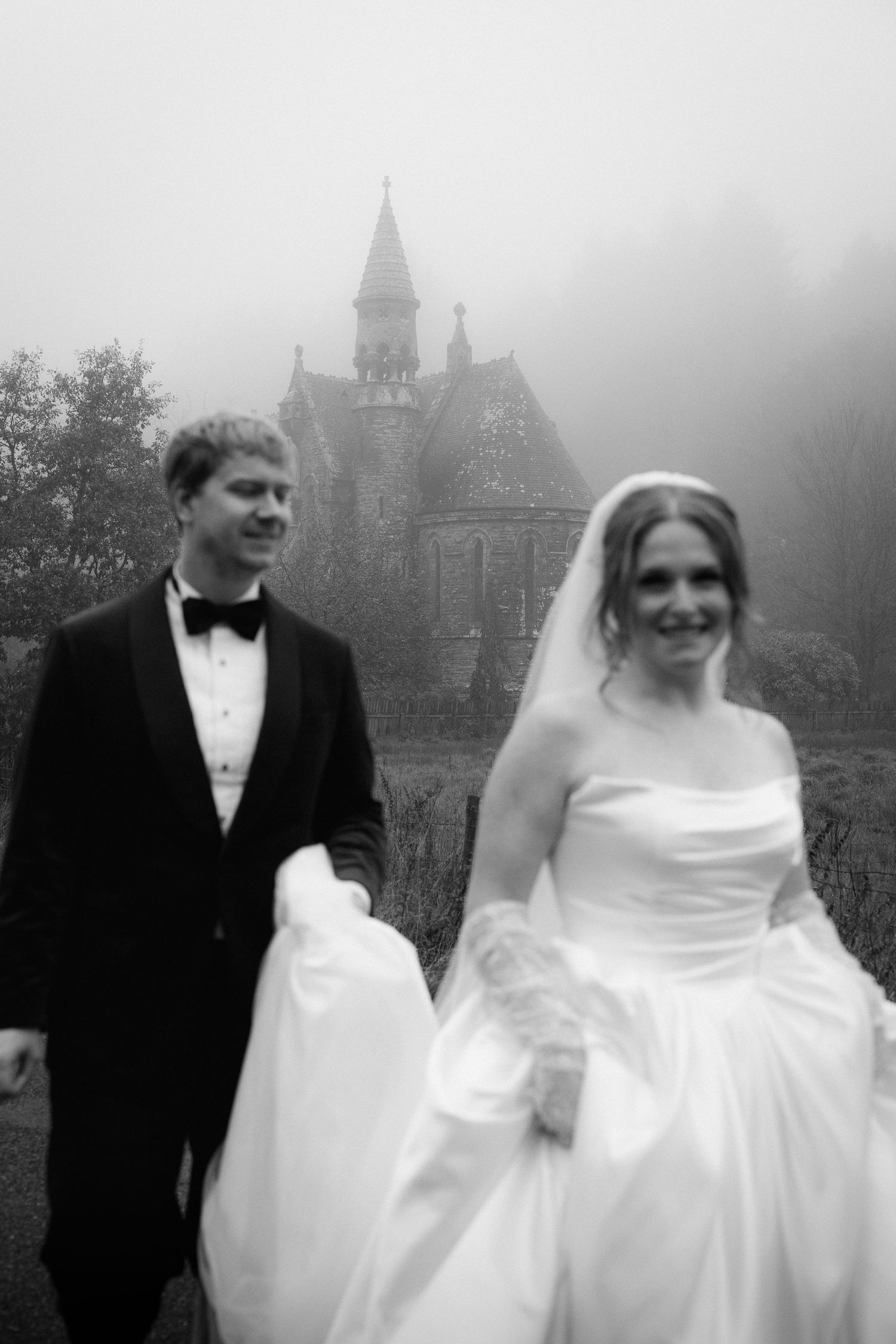 A black and white wedding photo sequence showing a couple walking and smiling in front of a misty gothic building.