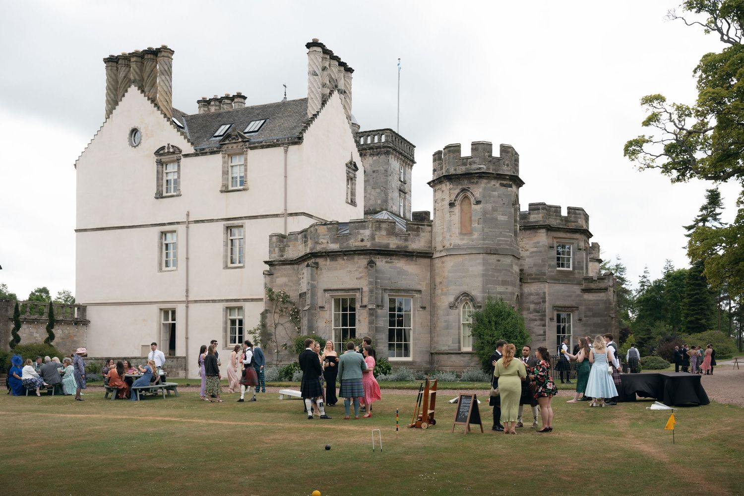 Historic castle building with turrets and stone architecture surrounded by green lawns and visitors on the grounds.