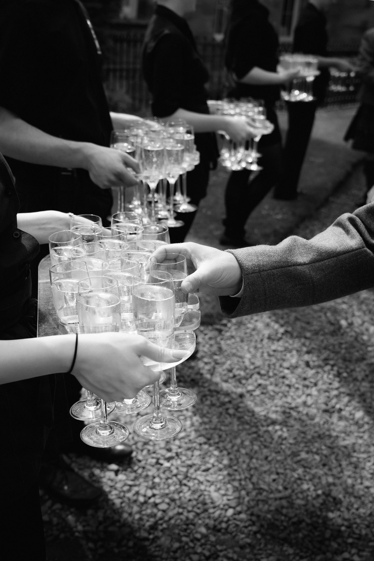 Hands passing champagne glasses during an elegant black and white reception celebration.