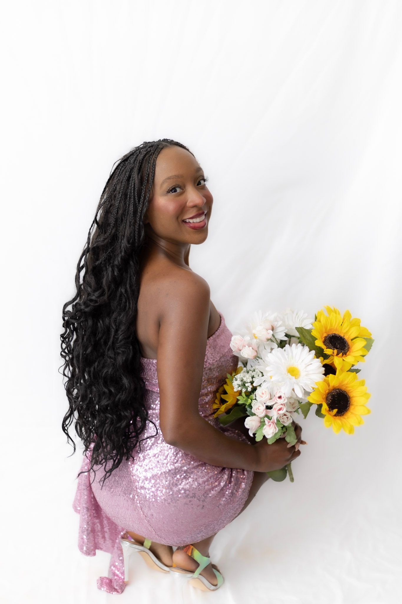 Smiling woman in pink sequin dress holding sunflower bouquet against white background.