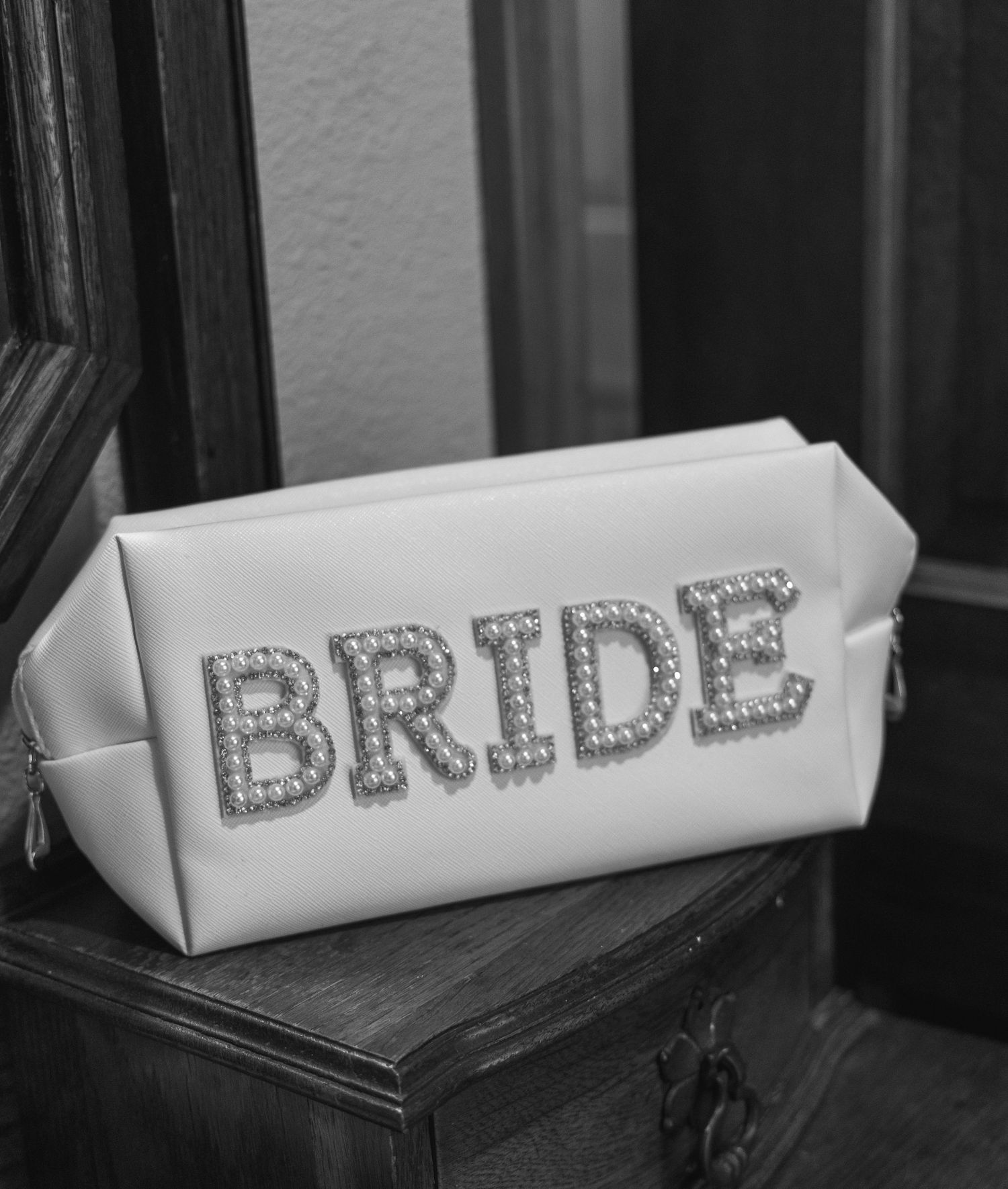 Black and white photo of a white leather bridal cosmetic bag with rhinestone BRIDE lettering.