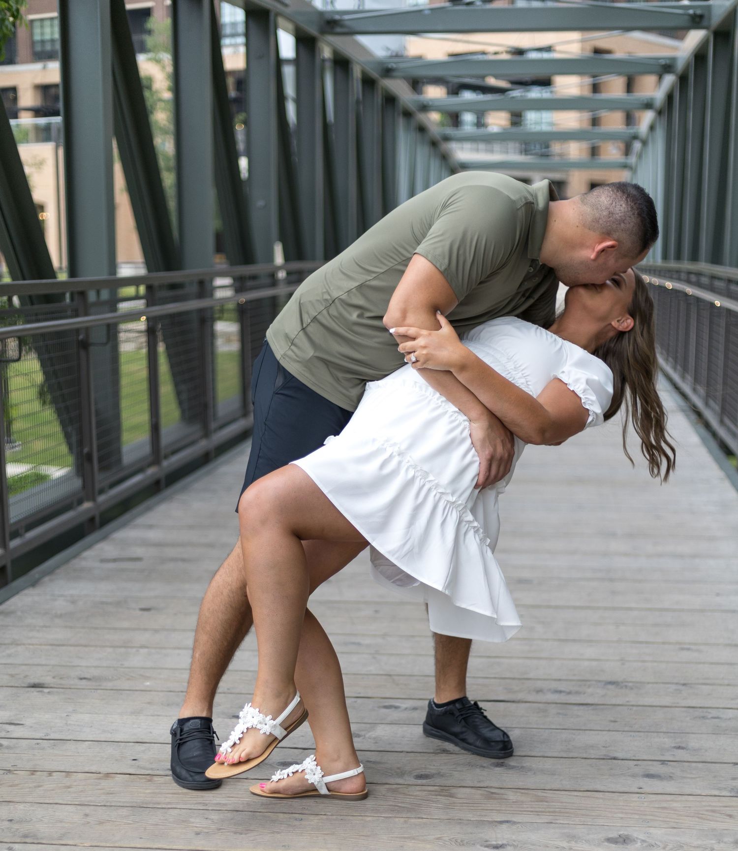 Romantic couple sharing a dip kiss on a bridge during their engagement photo session outdoors.