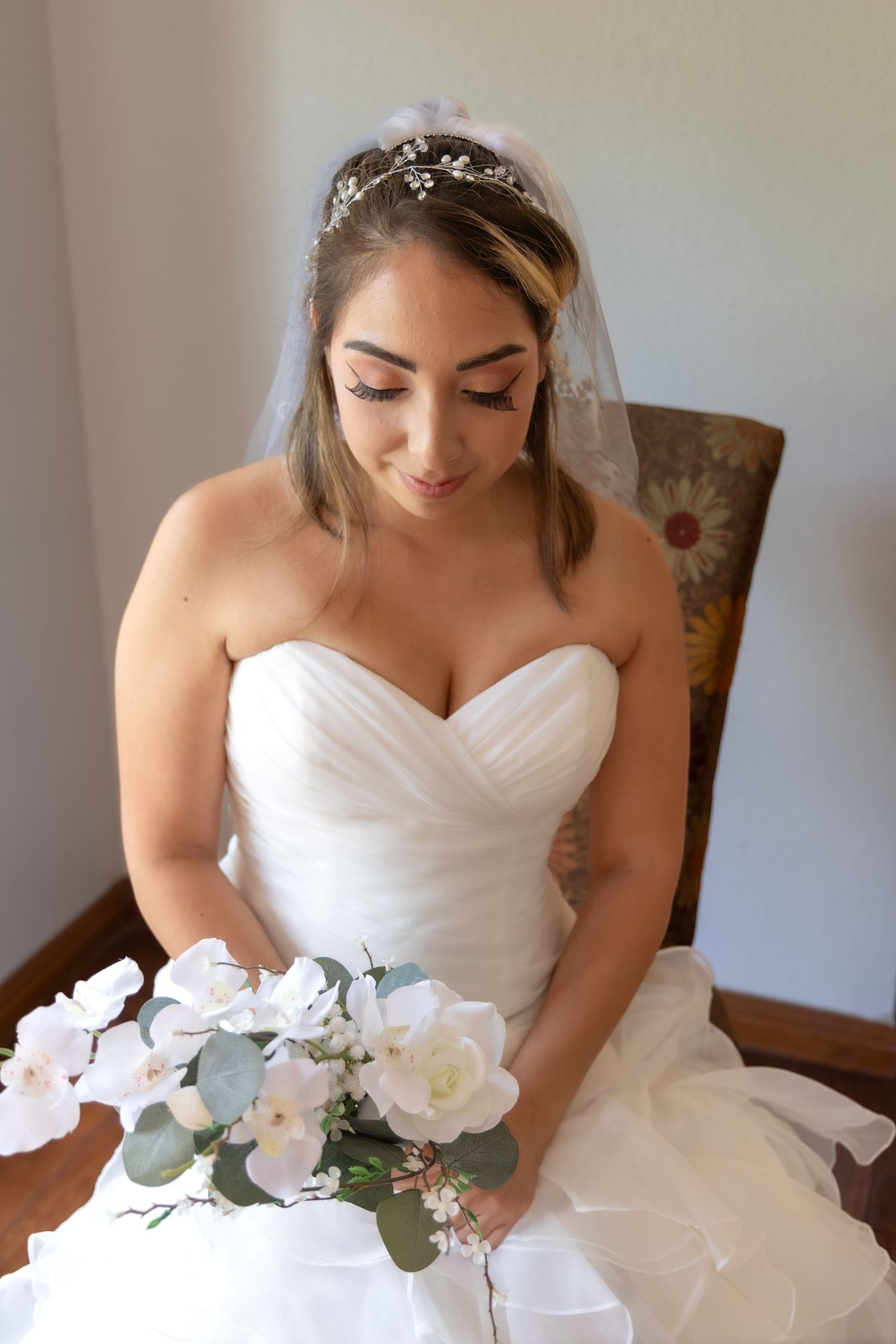 Beautiful bride in strapless white gown holding white rose bouquet with veil and floral headpiece.
