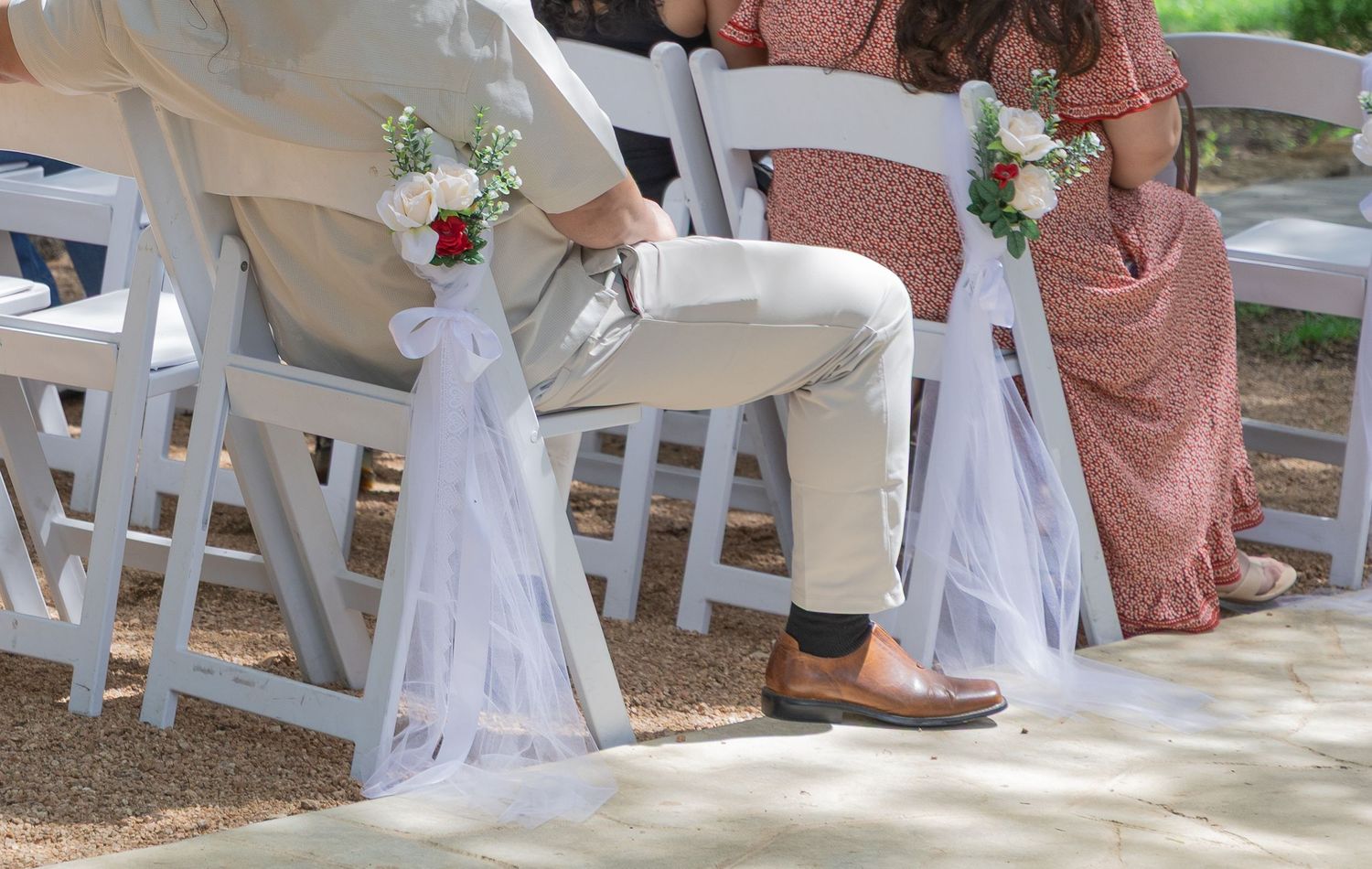 Wedding guests seated in white chairs decorated with white tulle and red rose floral accents.