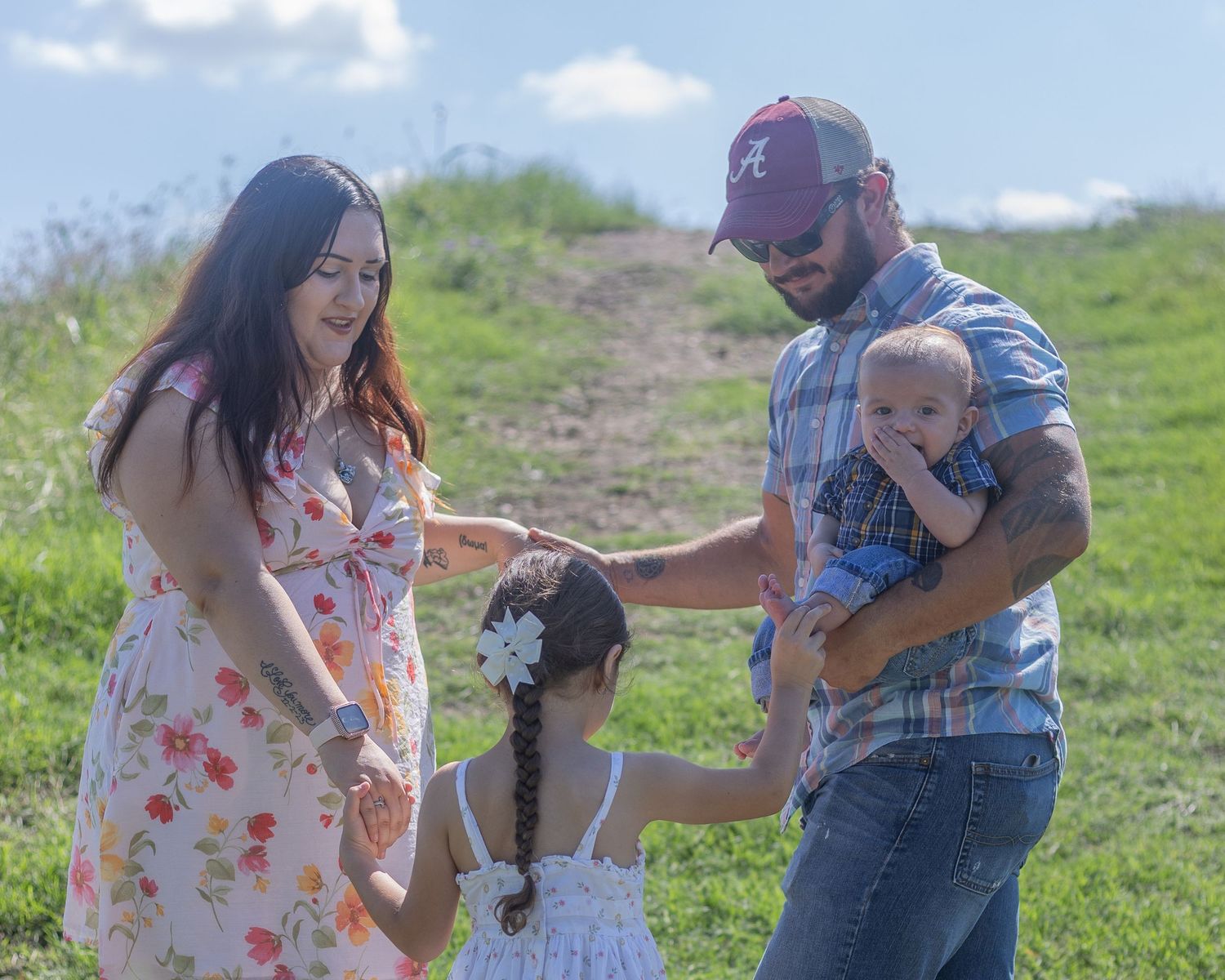 Happy family of four with young daughter and baby boy enjoy a sunny day on a green hillside.