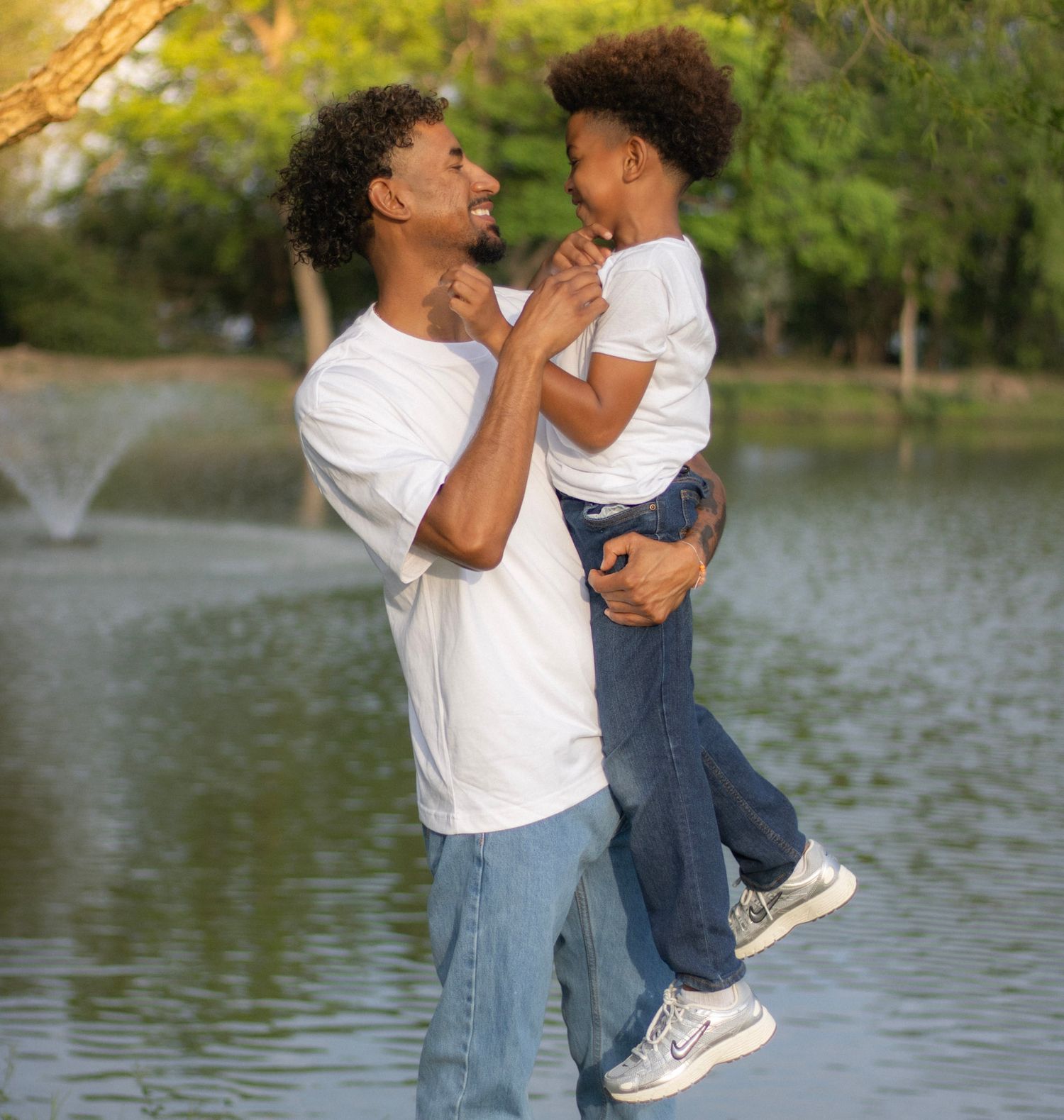 Father and son sharing a joyful moment by a pond, with the dad lifting the smiling boy.