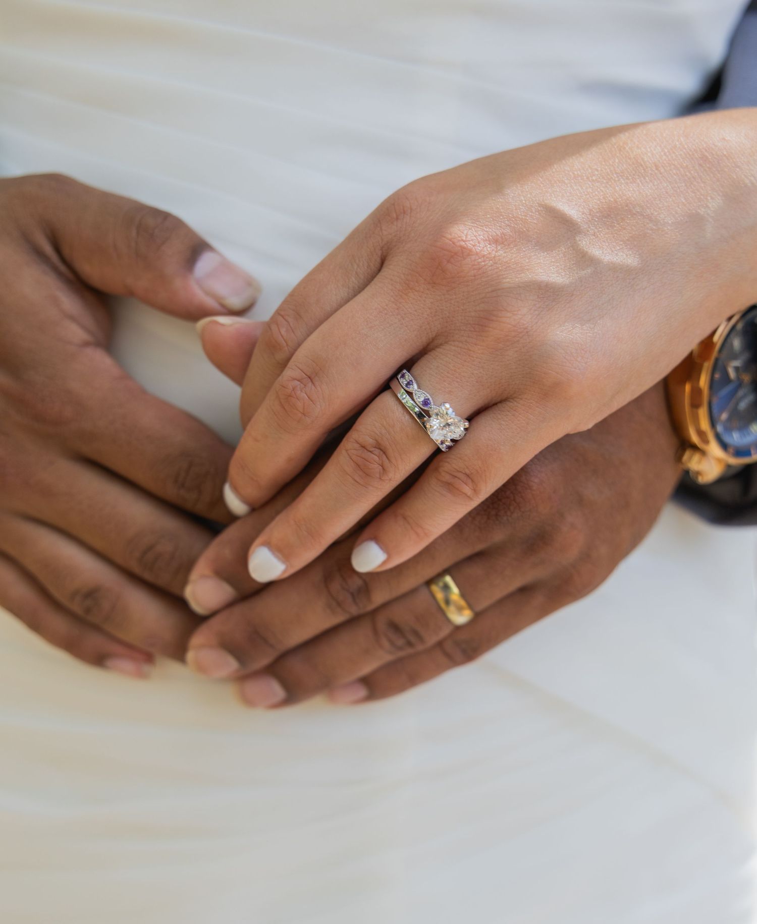 Close-up of newlywed couple's hands displaying diamond engagement ring set and groom's gold wedding band.
