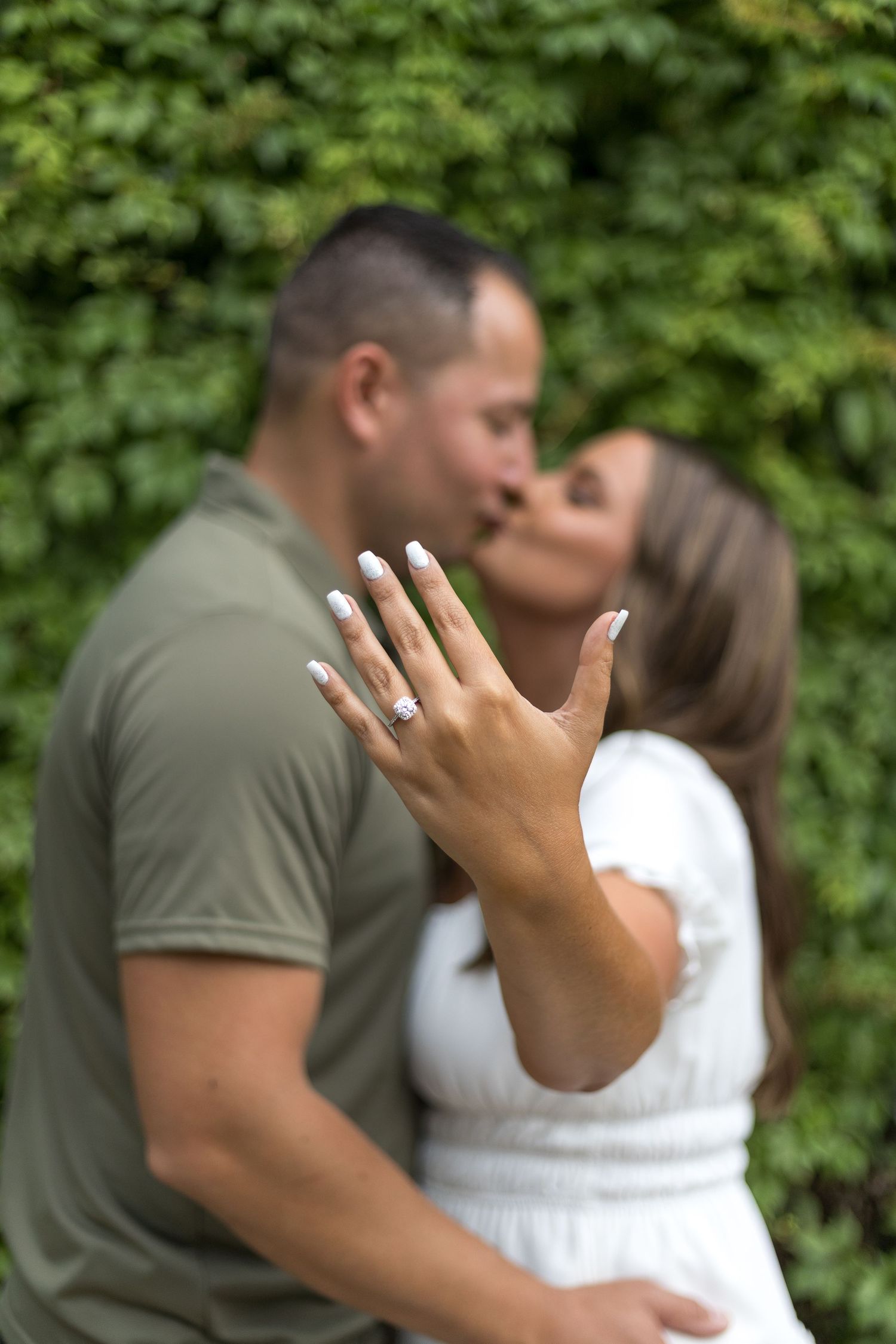 Newly engaged couple kissing while woman displays her diamond engagement ring in the foreground.