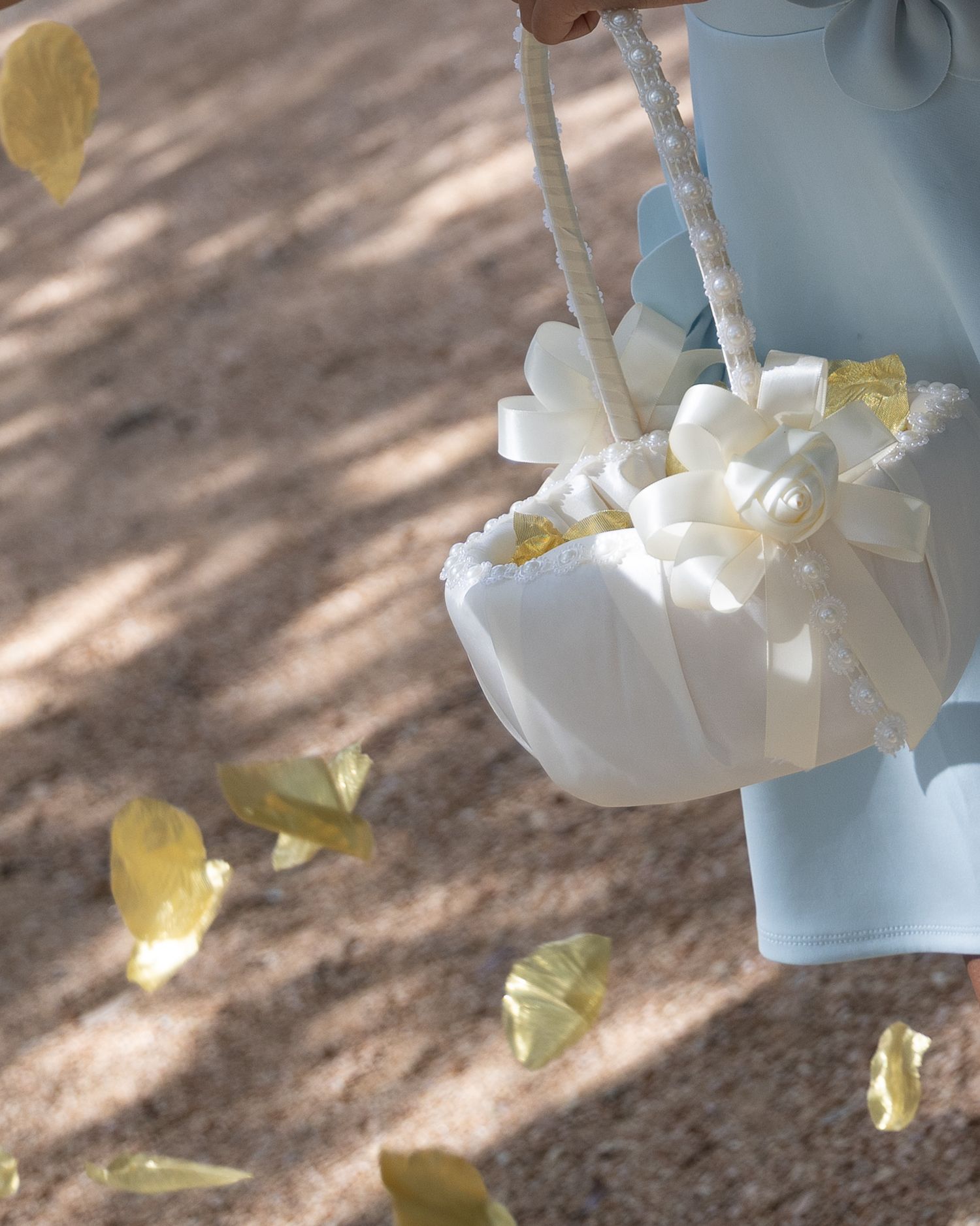 Flower girl basket with white ribbon bow and yellow petals scattered on ground at wedding ceremony.