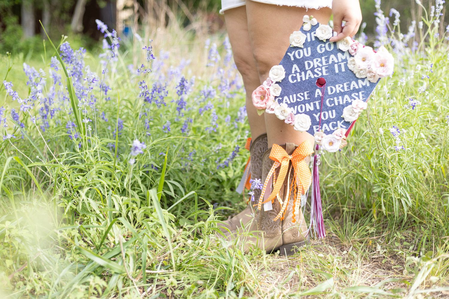 Decorated graduation cap with inspirational quote displayed in wildflower field.