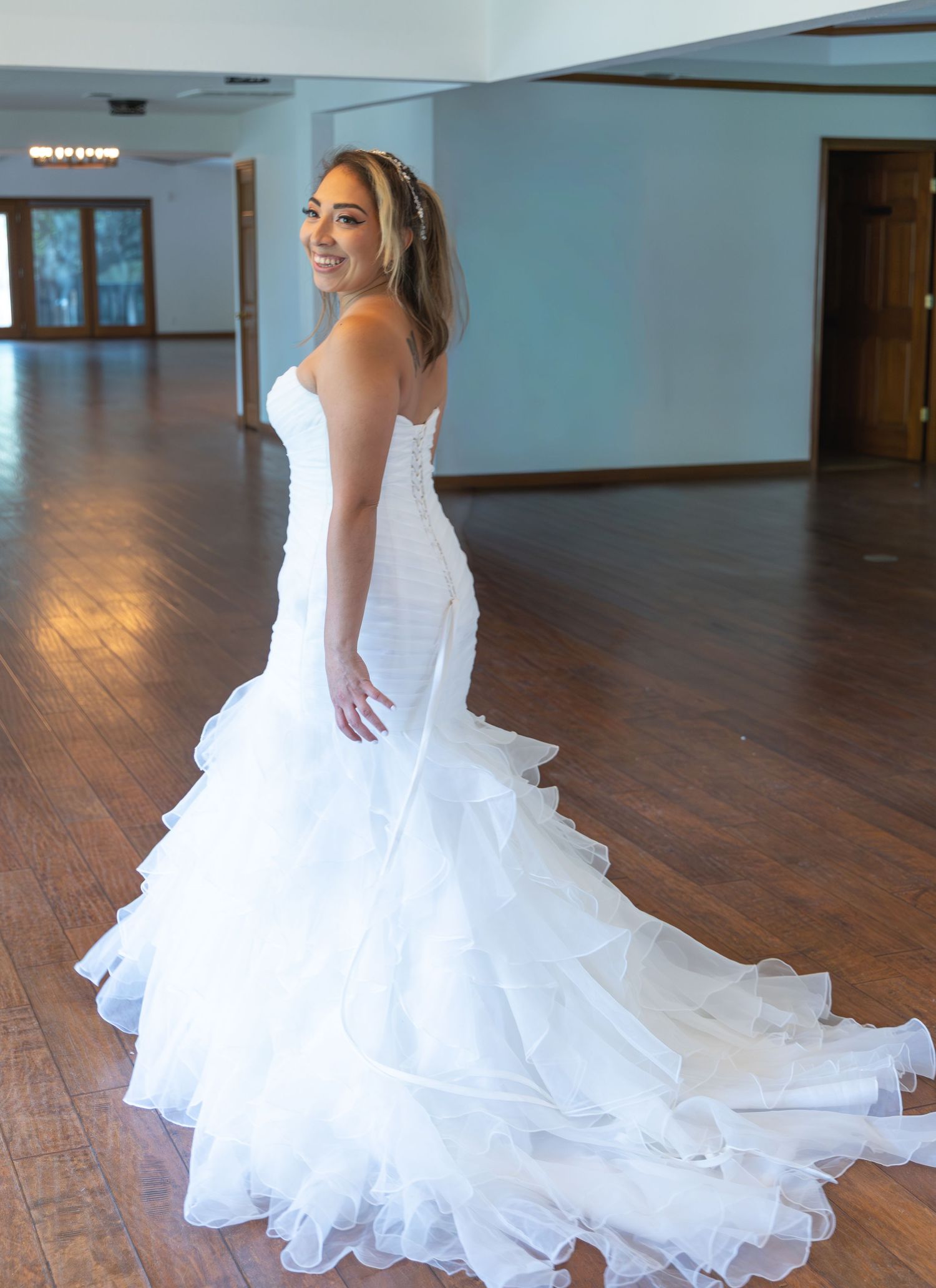 Bride in a strapless mermaid wedding gown with ruffled train posing in a wooden reception hall.
