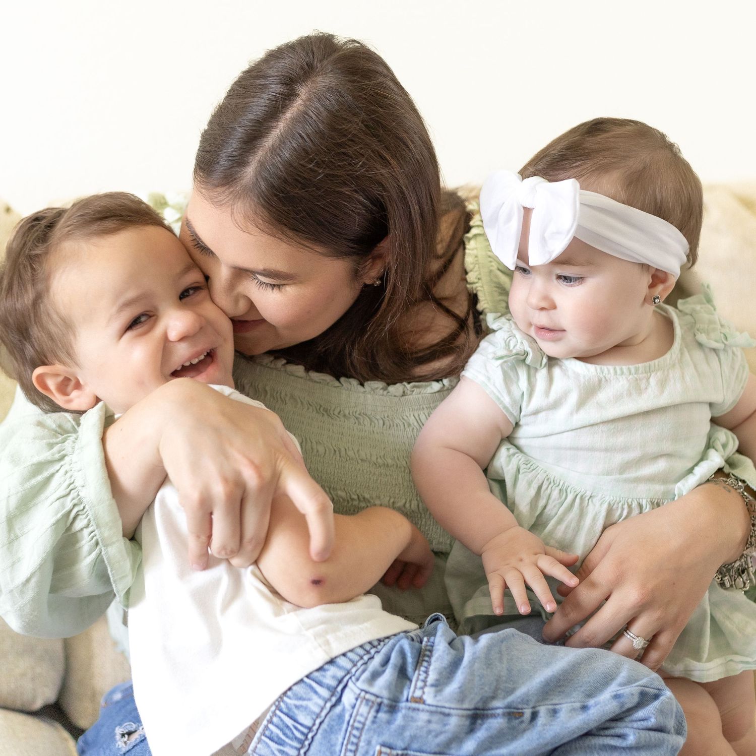 Young mother smiling and cuddling two happy babies dressed in matching green outfits.