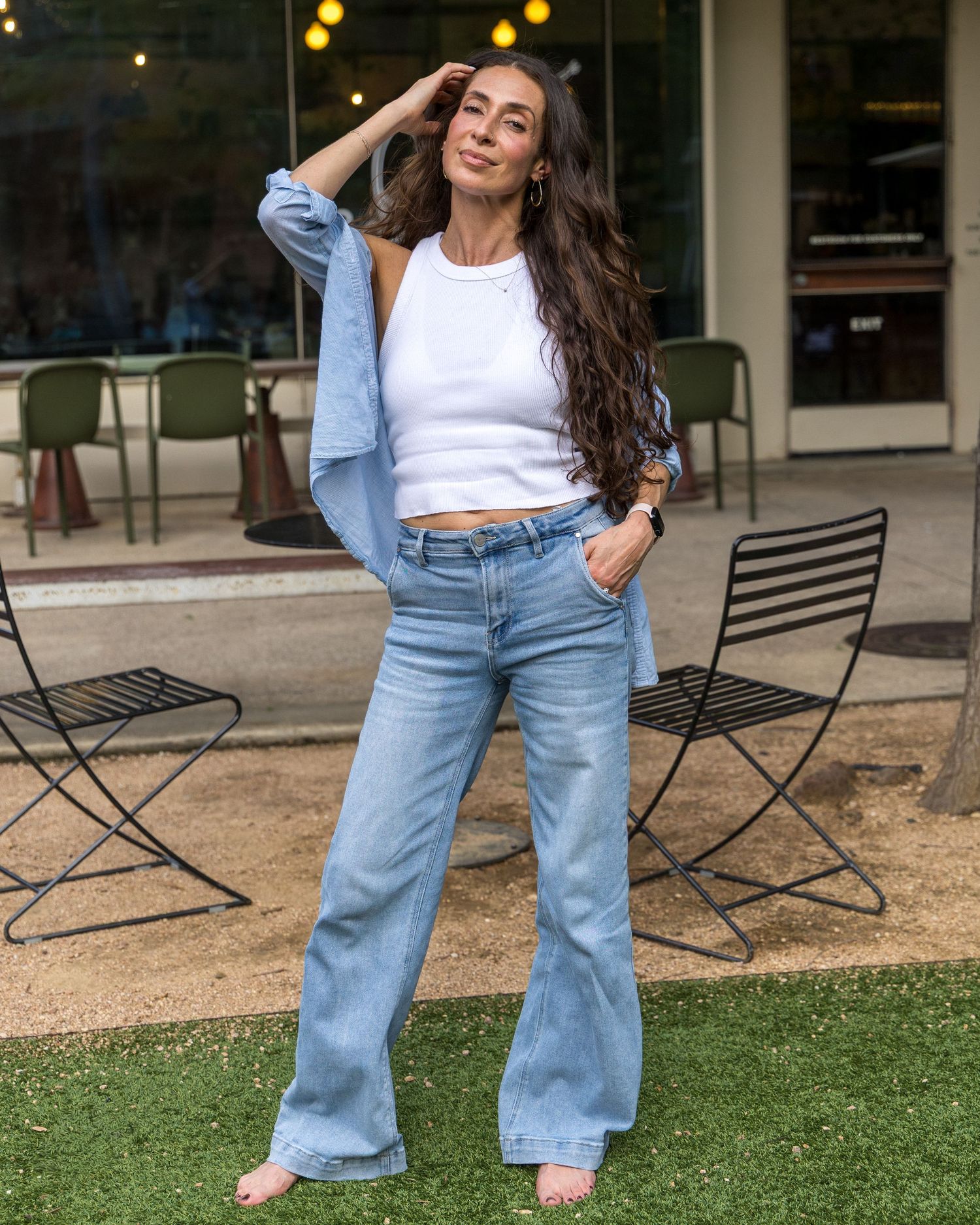 Stylish woman poses in white crop top, blue button-down shirt, and wide-leg light wash jeans outdoors.
