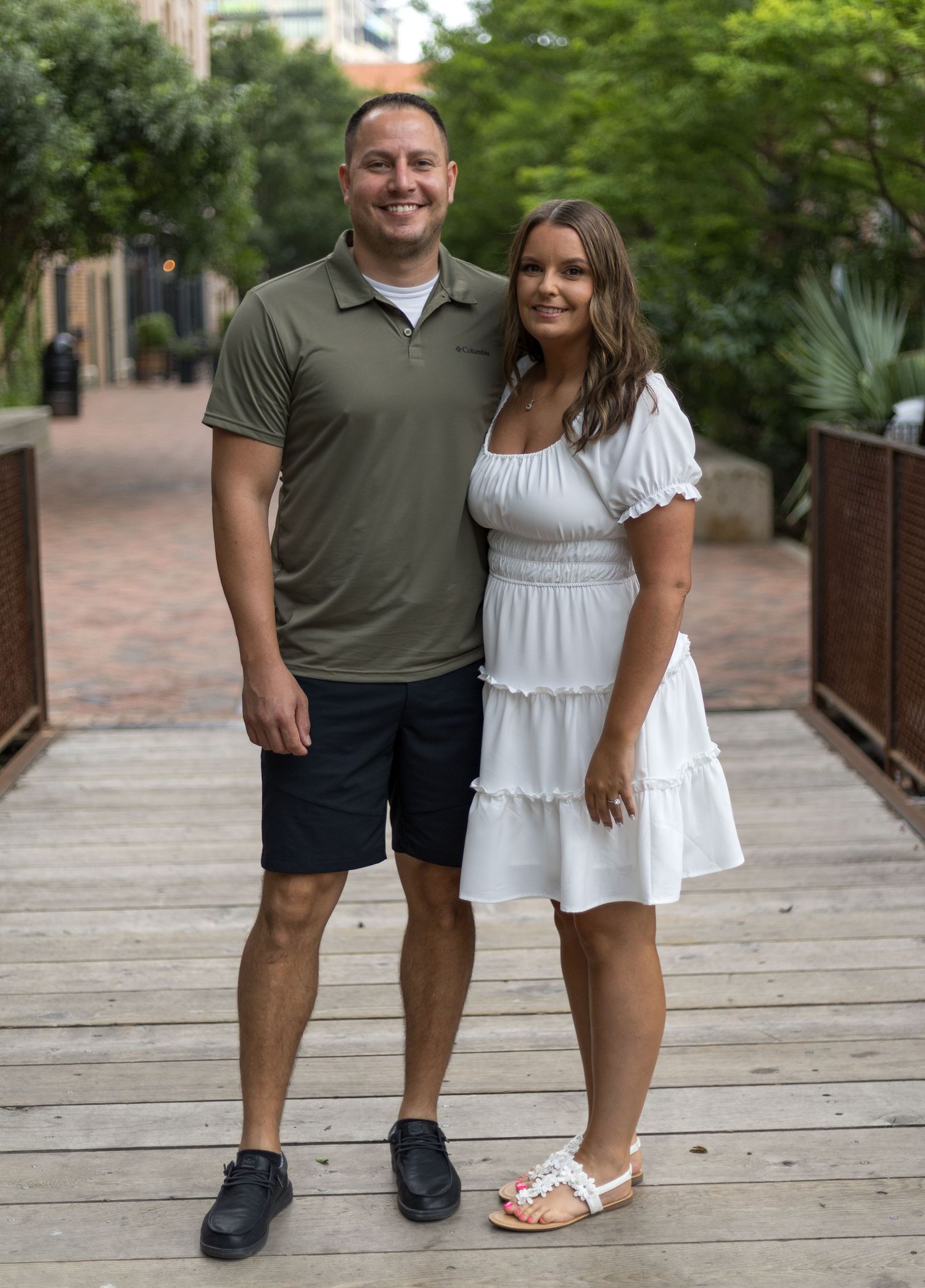 Smiling couple standing together on wooden bridge in urban outdoor setting.