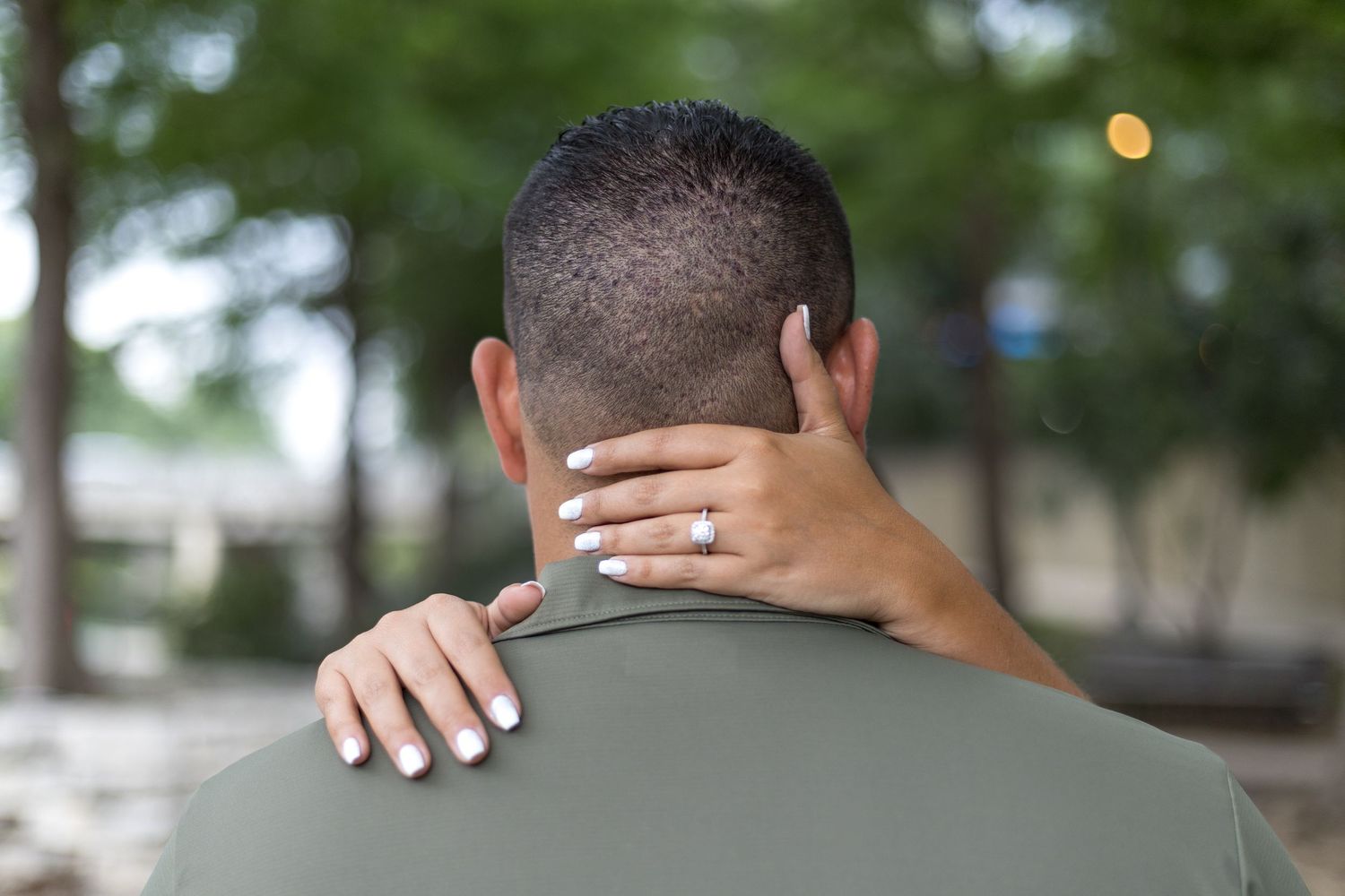 Close-up back view of woman placing her hand with engagement ring on her partners shoulder.