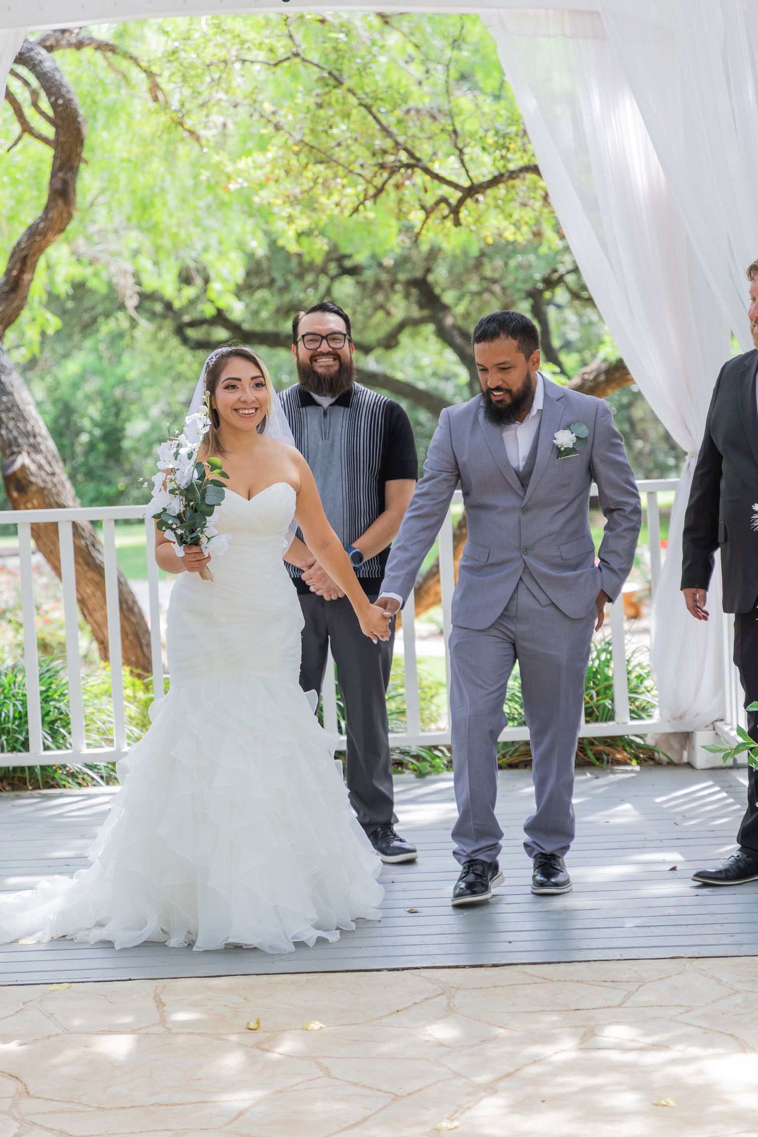 Newlyweds walk hand in hand down aisle after outdoor wedding ceremony under white draped pergola.