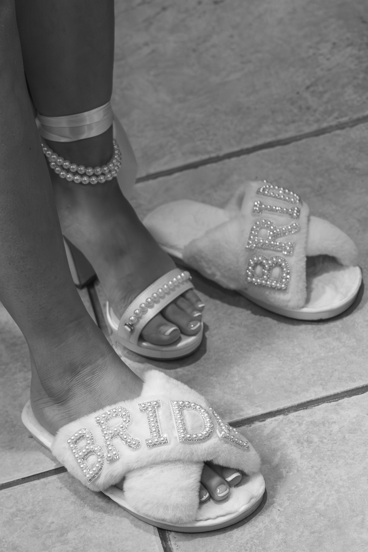 Black and white photo of bride wearing fluffy pearl-embellished BRIDE slides and pearl anklet bracelet.