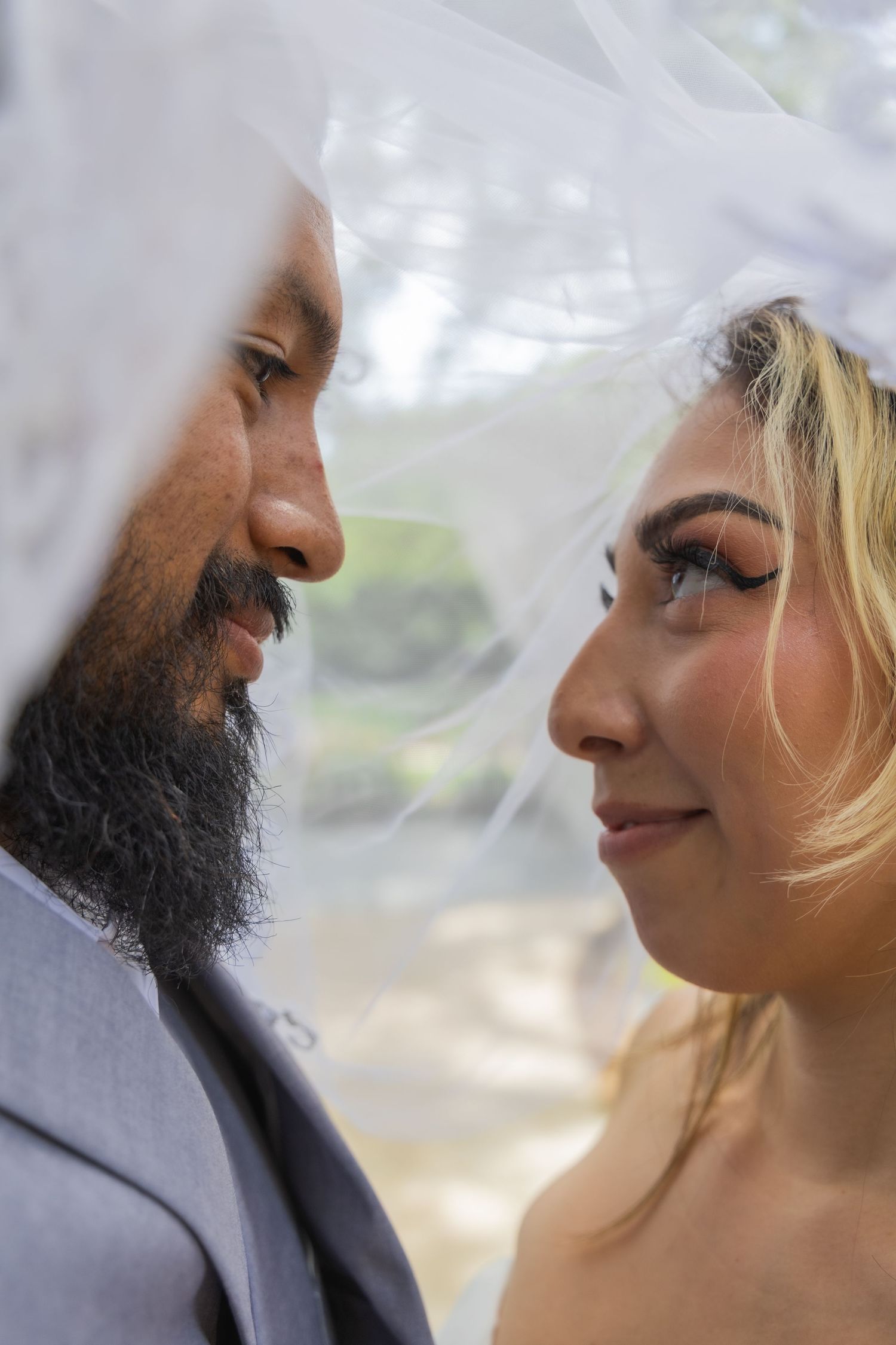Intimate close-up portrait of bride and groom gazing at each other beneath a sheer white bridal veil.