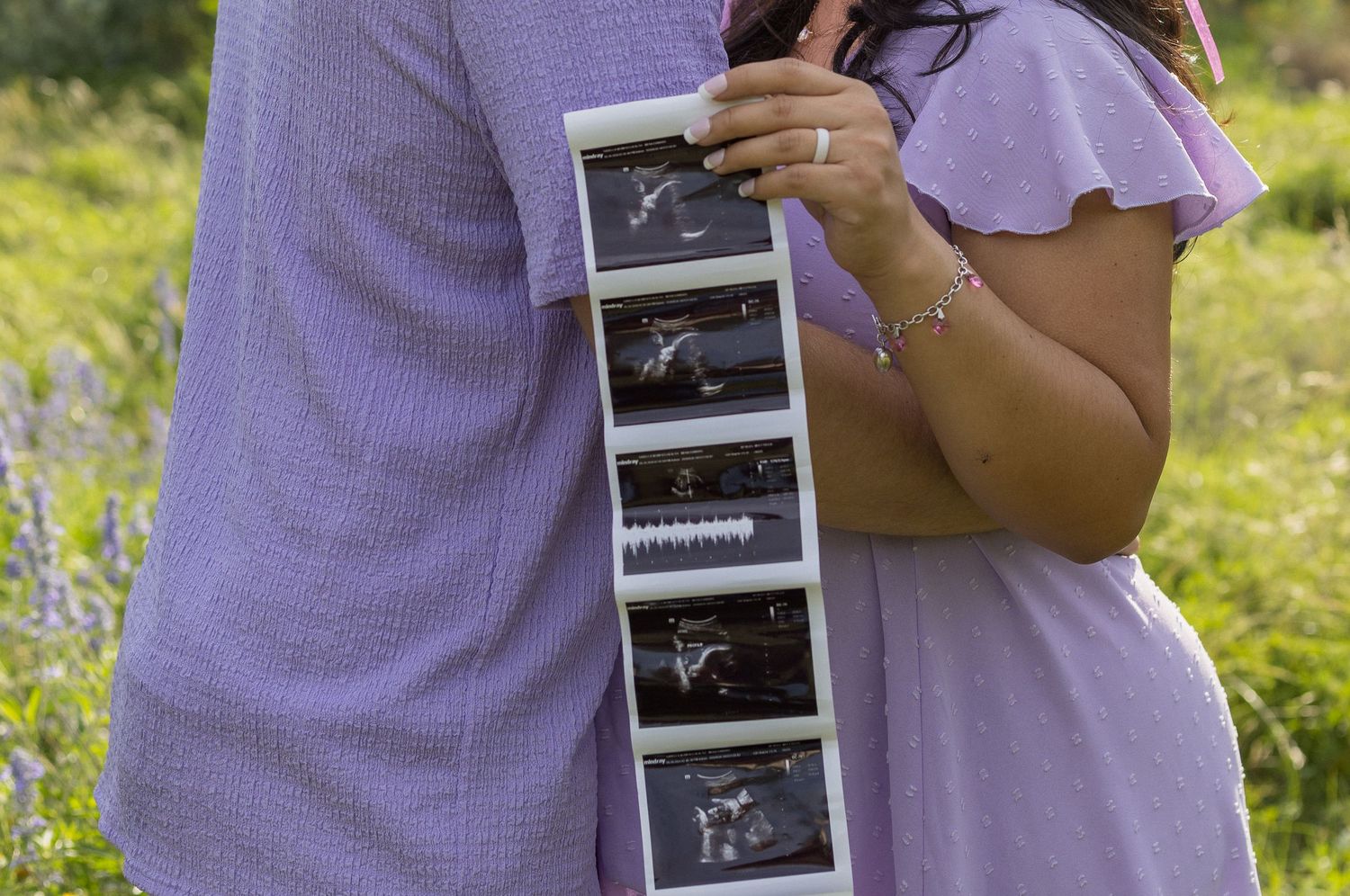 Couple holding ultrasound photos in a purple wildflower field during maternity photo session.