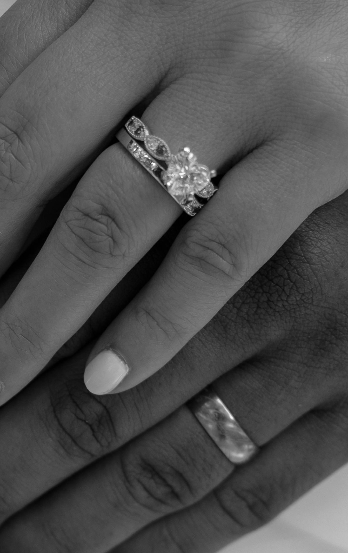 Close-up black and white photo of couple's hands showing diamond engagement ring, wedding band, and groom's simple ring.