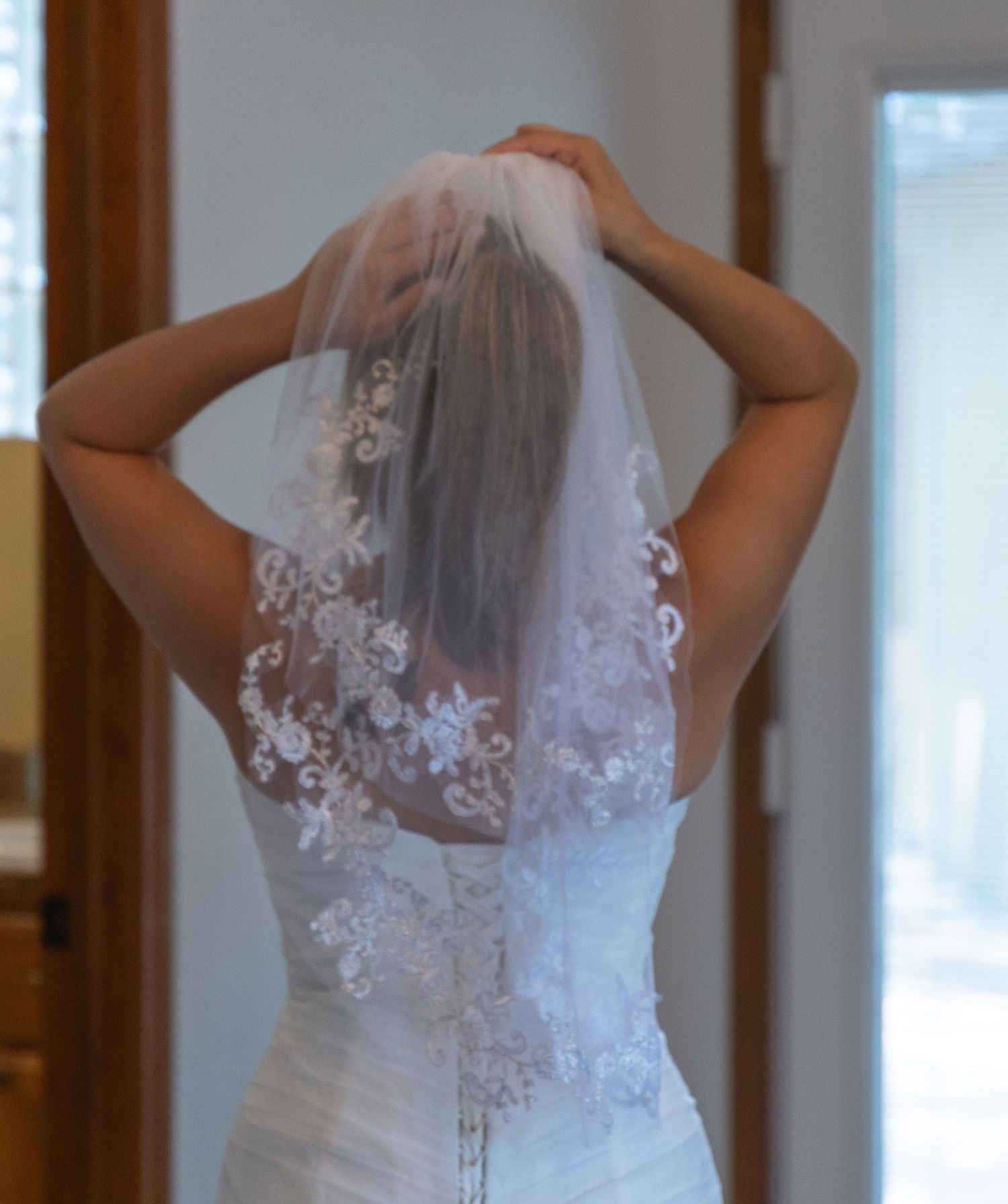 Back view of a bride adjusting her lace-trimmed veil over an elegant lace wedding dress.