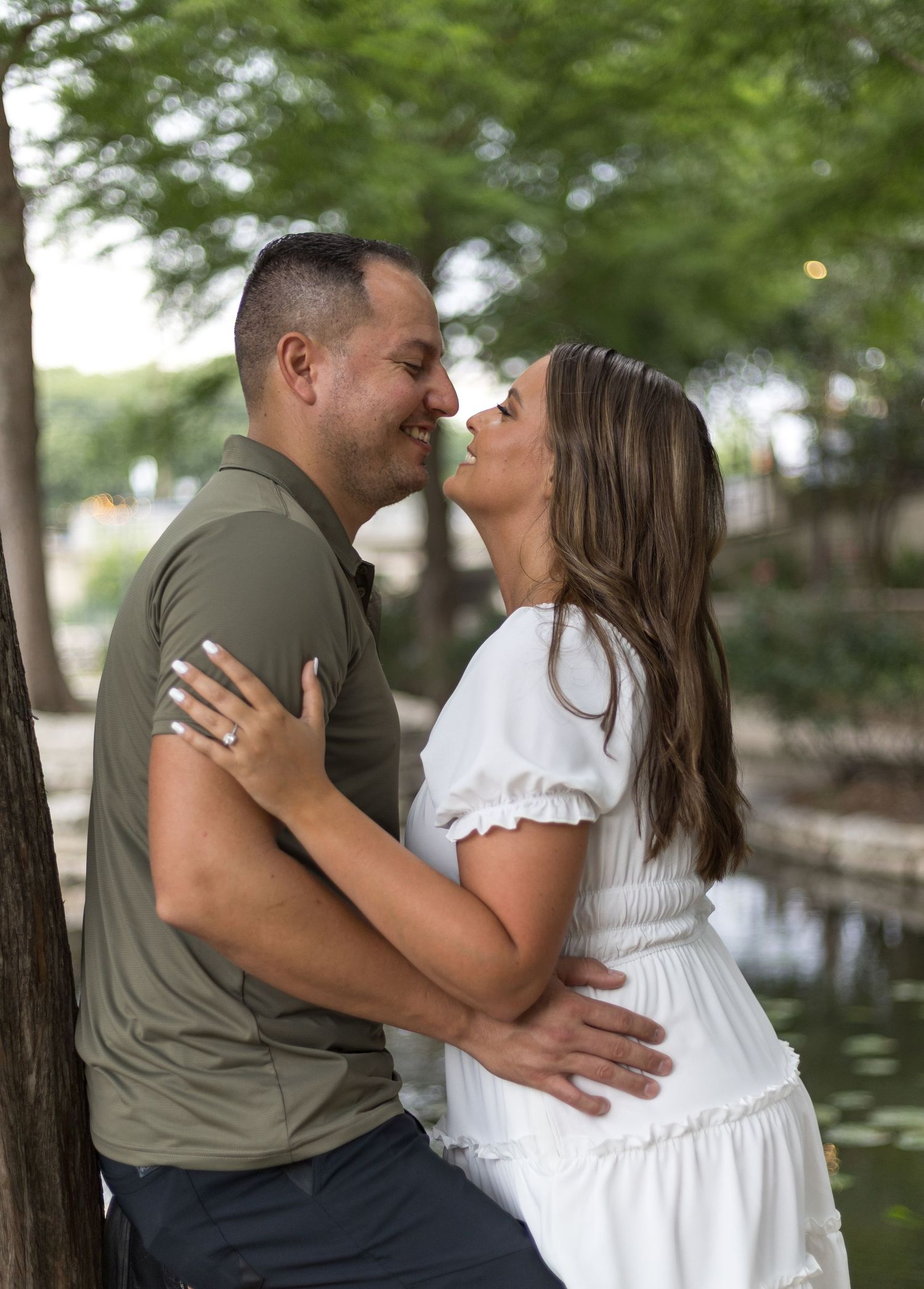 Couple sharing a romantic moment about to kiss near a tree by a peaceful waterway.