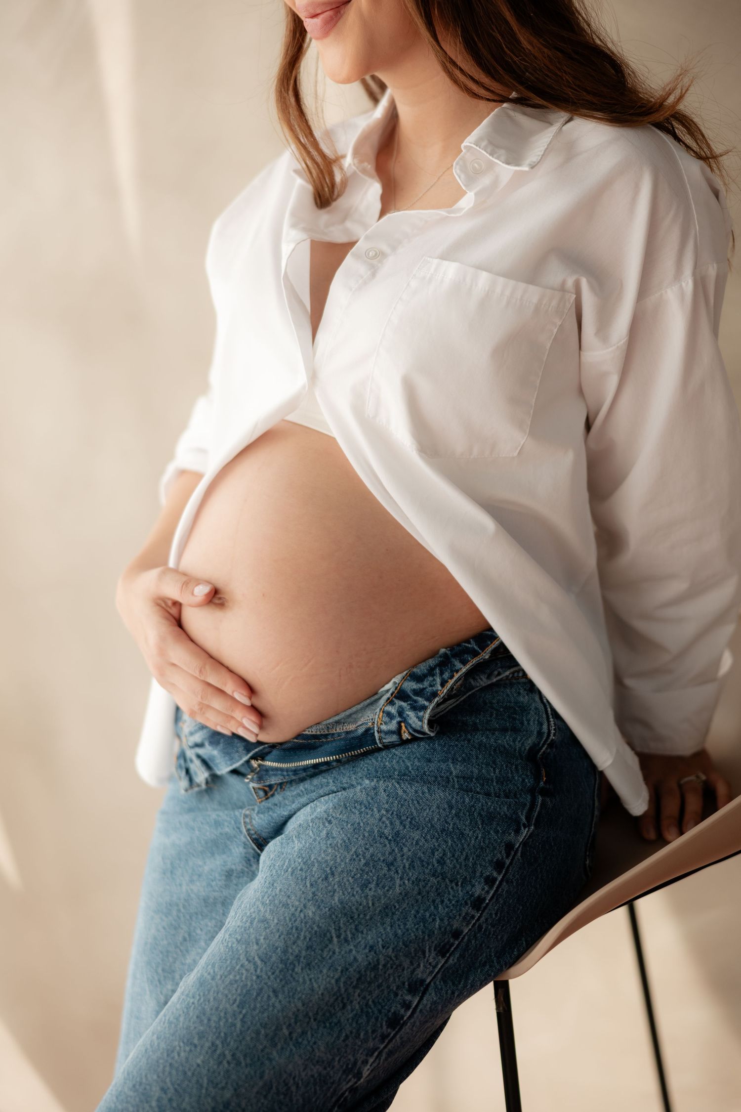 Close-up of pregnant woman in white shirt and jeans gently cradling her bare belly.