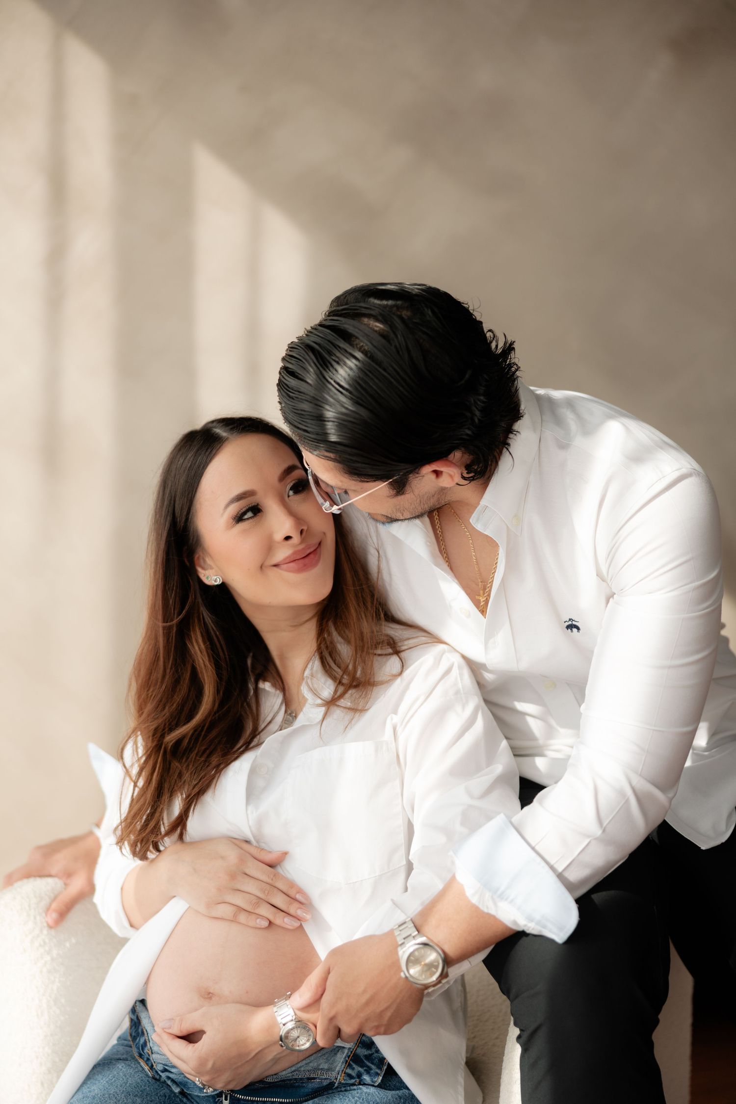 Couple expecting baby, man kissing pregnant woman's head while she smiles and holds bump.