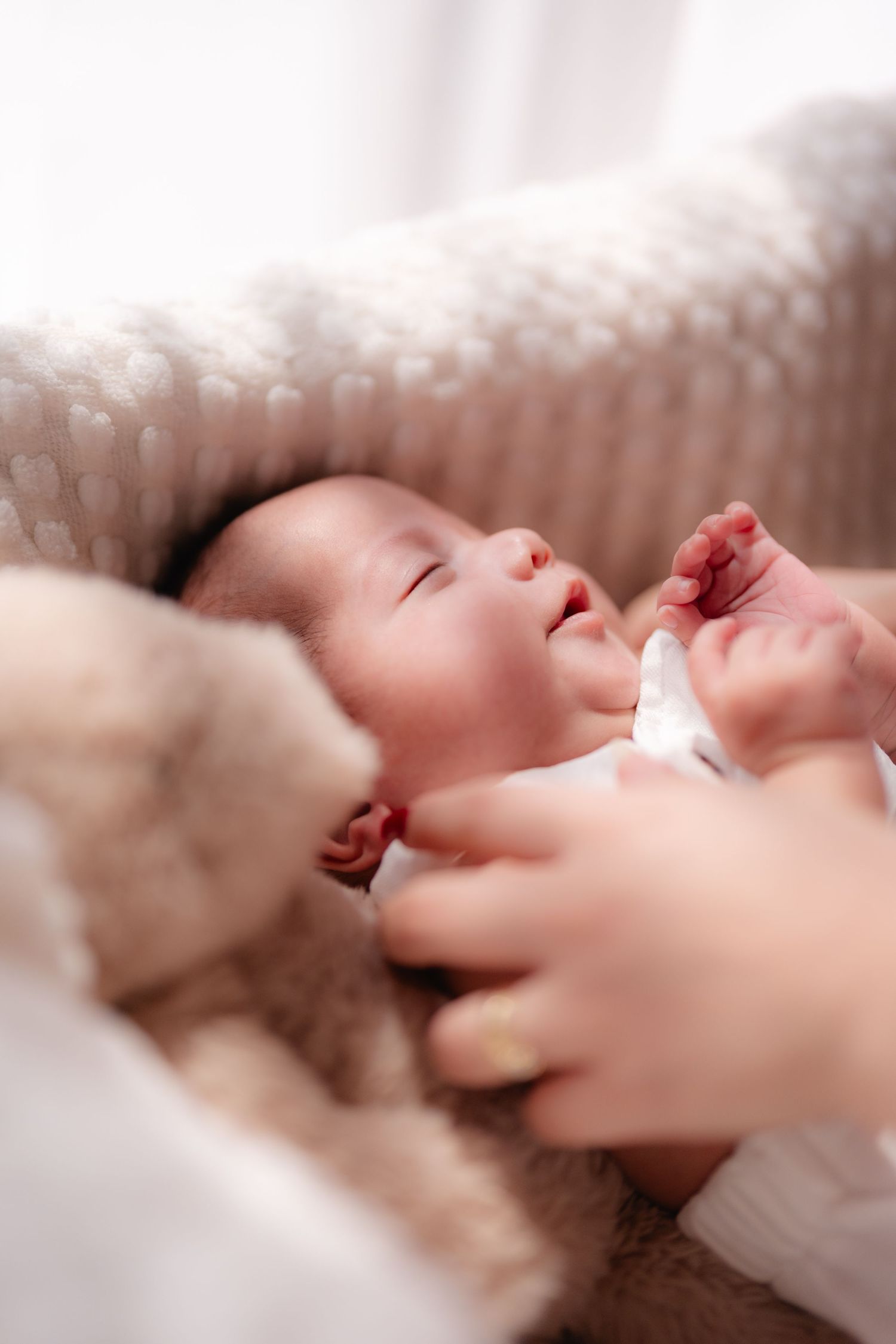 Newborn baby lying peacefully in a soft blanket, eyes closed, with tiny hands visible in warm natural light.