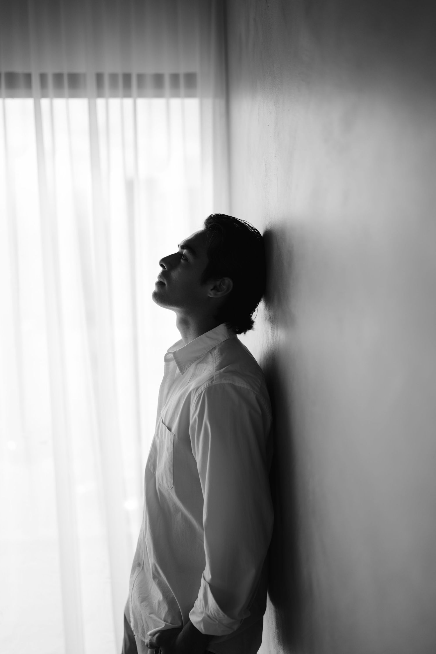 Black and white photo of man in white shirt leaning against wall, looking upward.