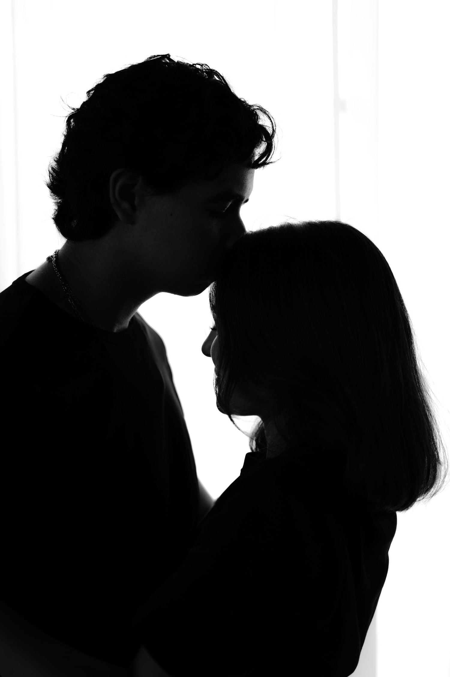 Romantic black and white silhouette of a couple sharing an intimate moment, backlit by soft window light.