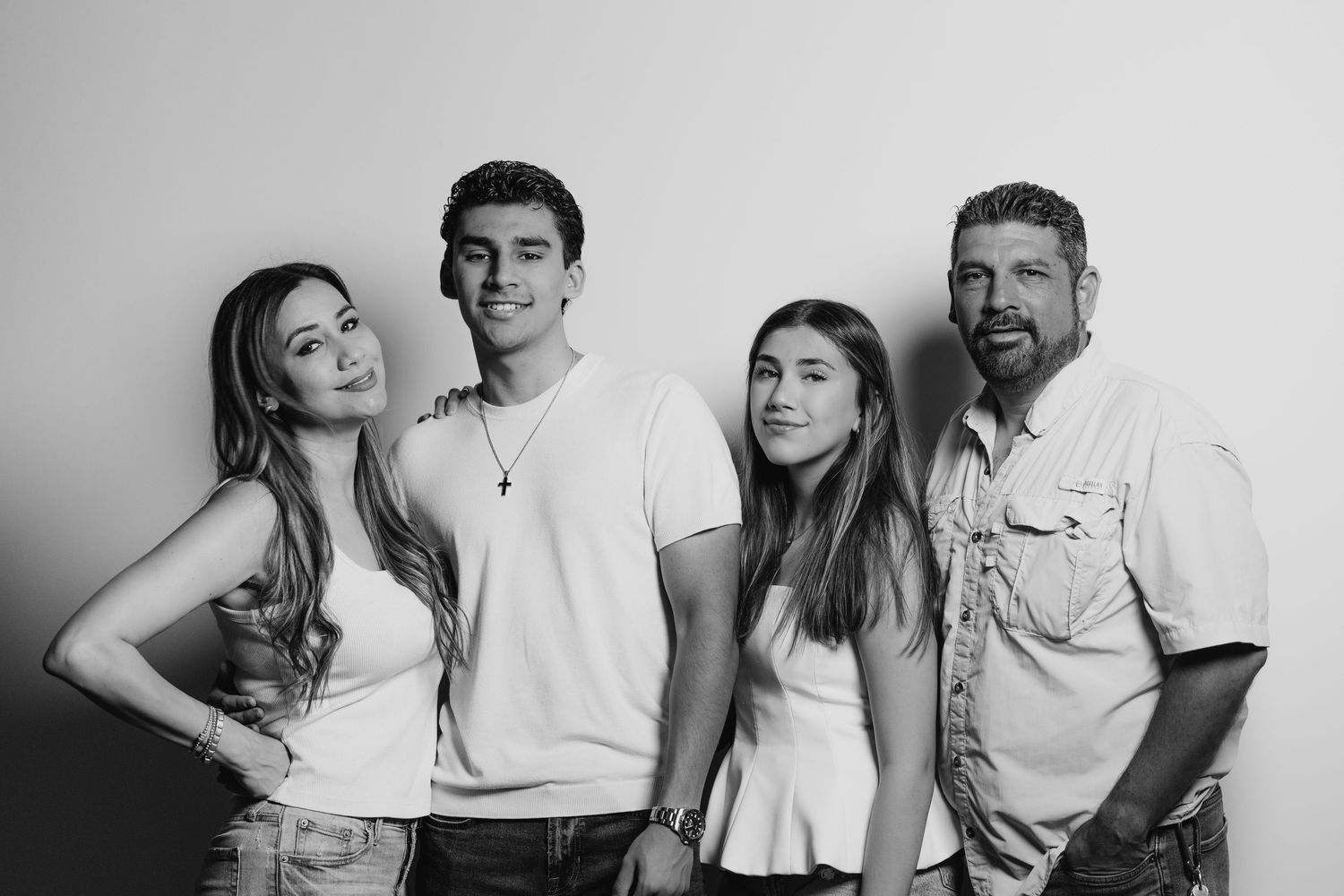 Black and white photo of a smiling family of four posing casually against a light background.