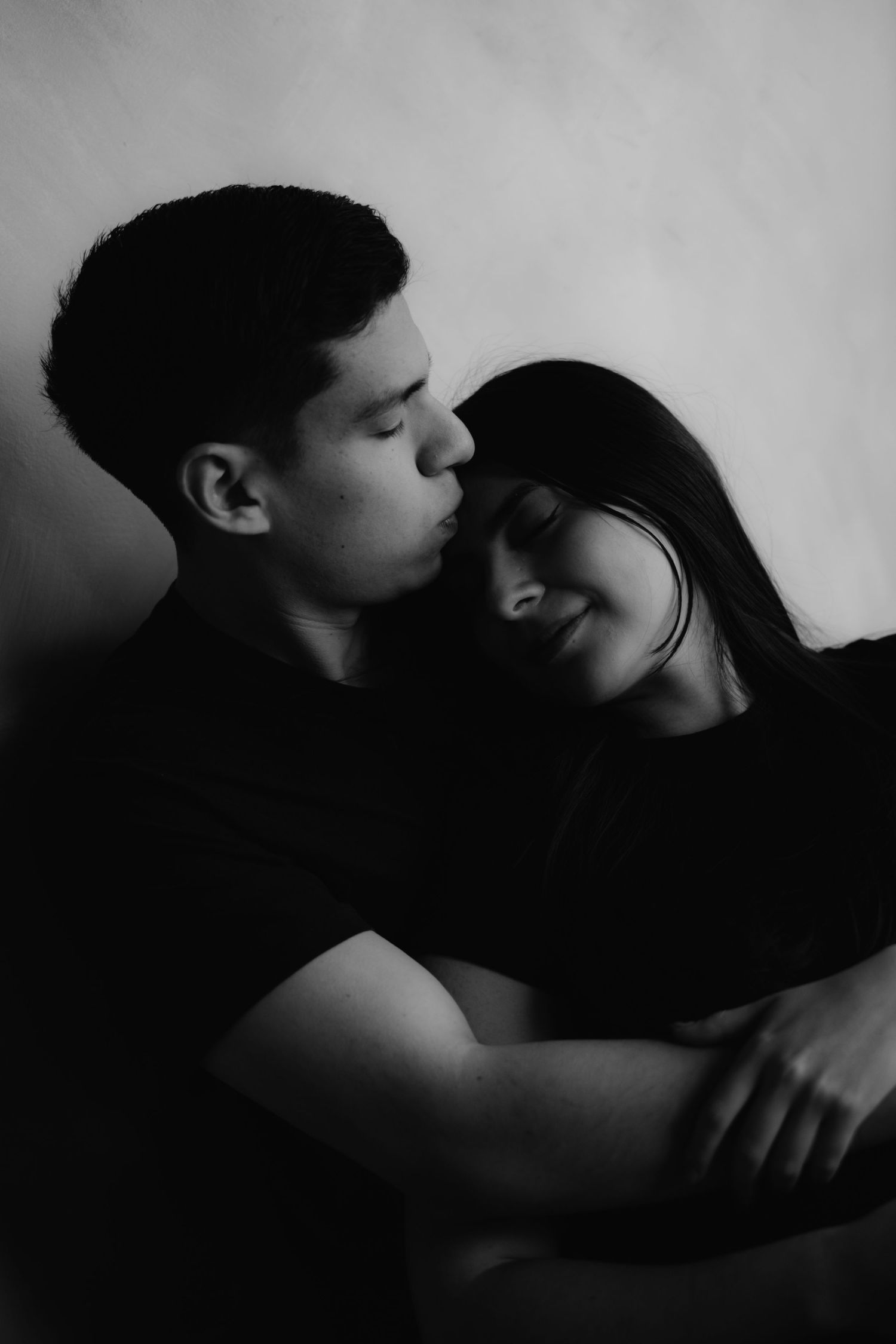 Tender black and white portrait of a young couple embracing, man kissing womans forehead gently.